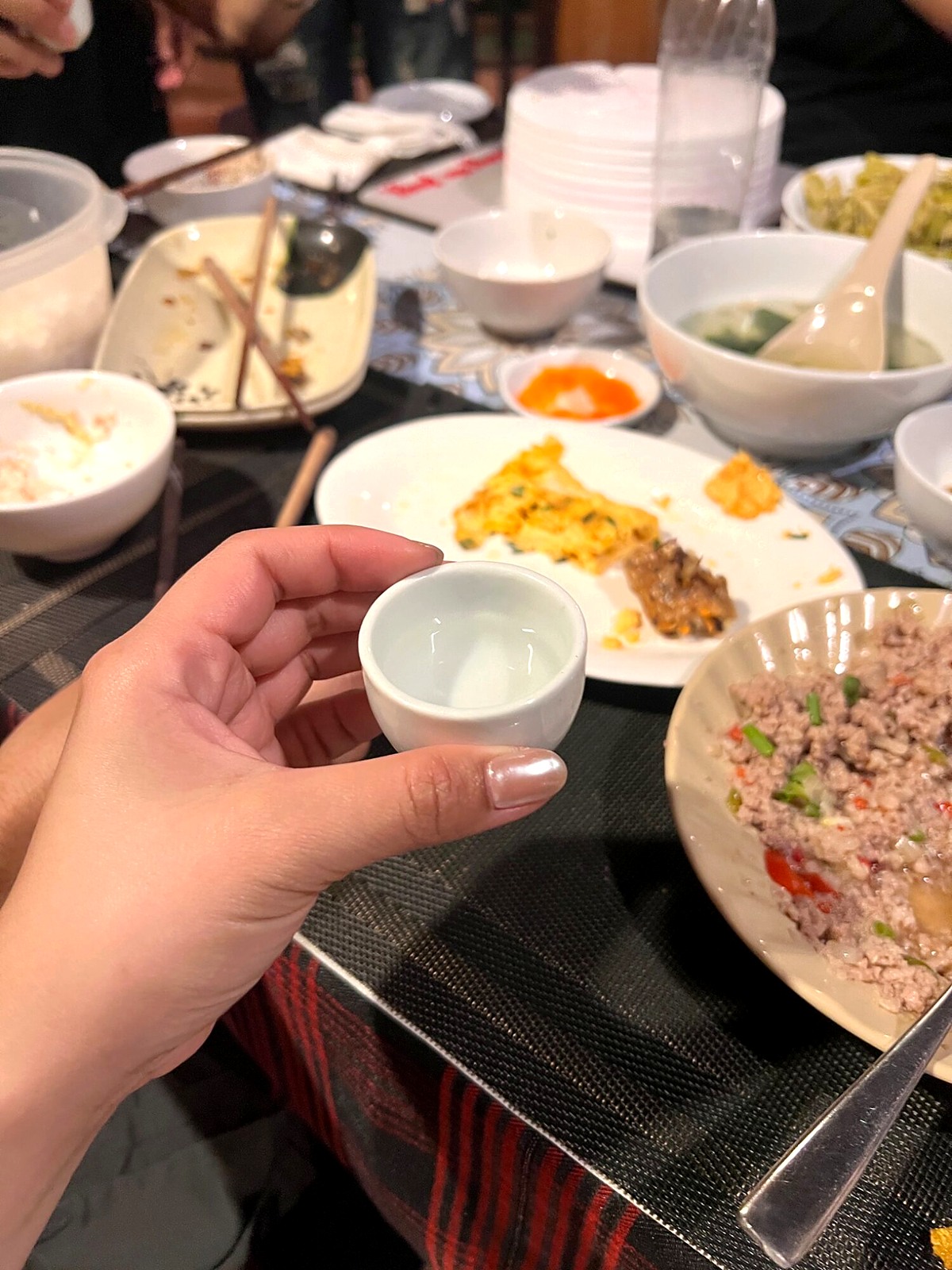 A hand holding a small cup of happy water beside dinner plates