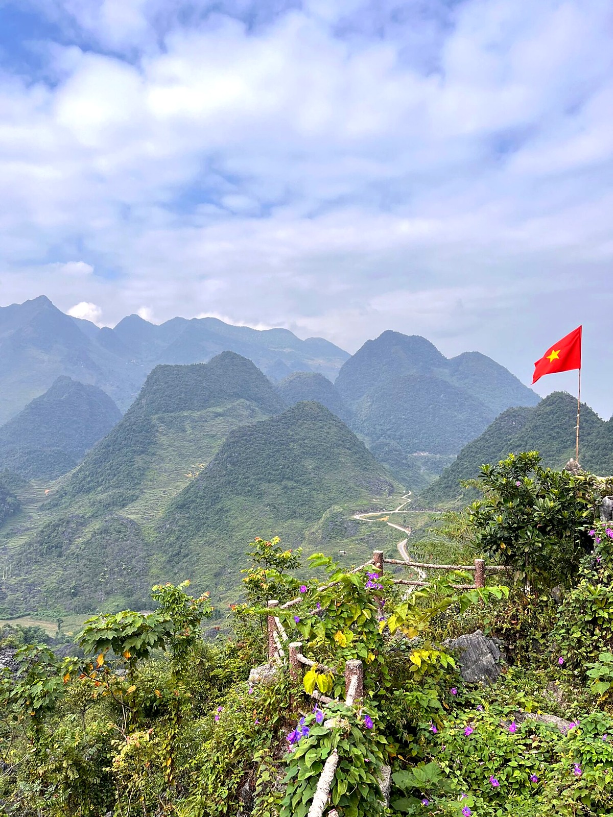 Layered mountain peaks beneath a blue sky and a Vietnamese flag