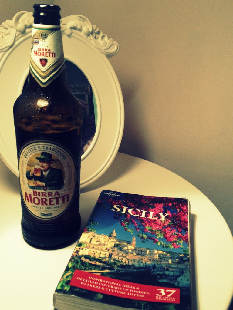 A well-worn Lonely Planet Sicily guidebook next to a bottle of Birra Moretti on a white table