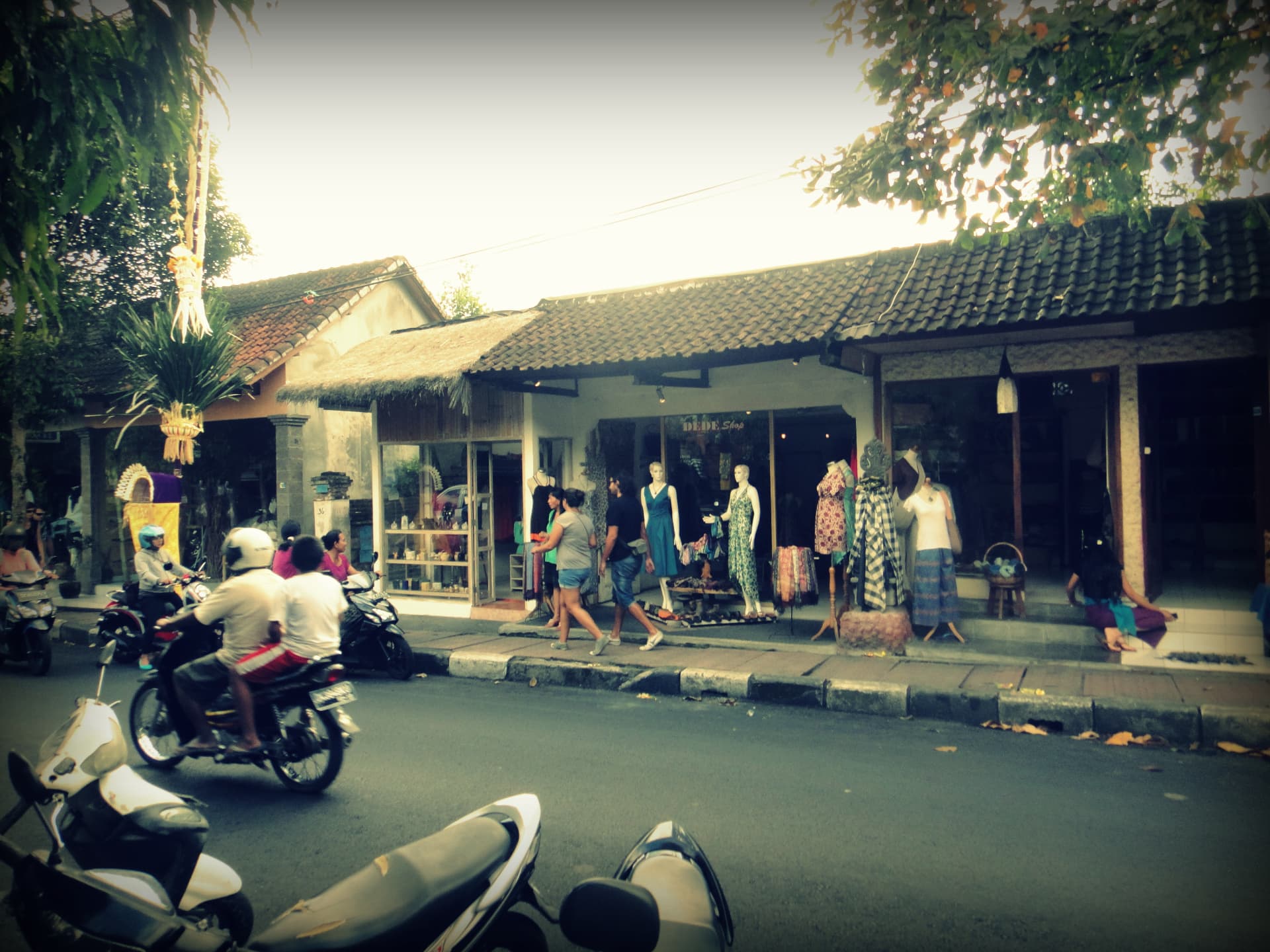 An Ubud street lined with small shops and boutiques, scooters passing and offerings by the roadside