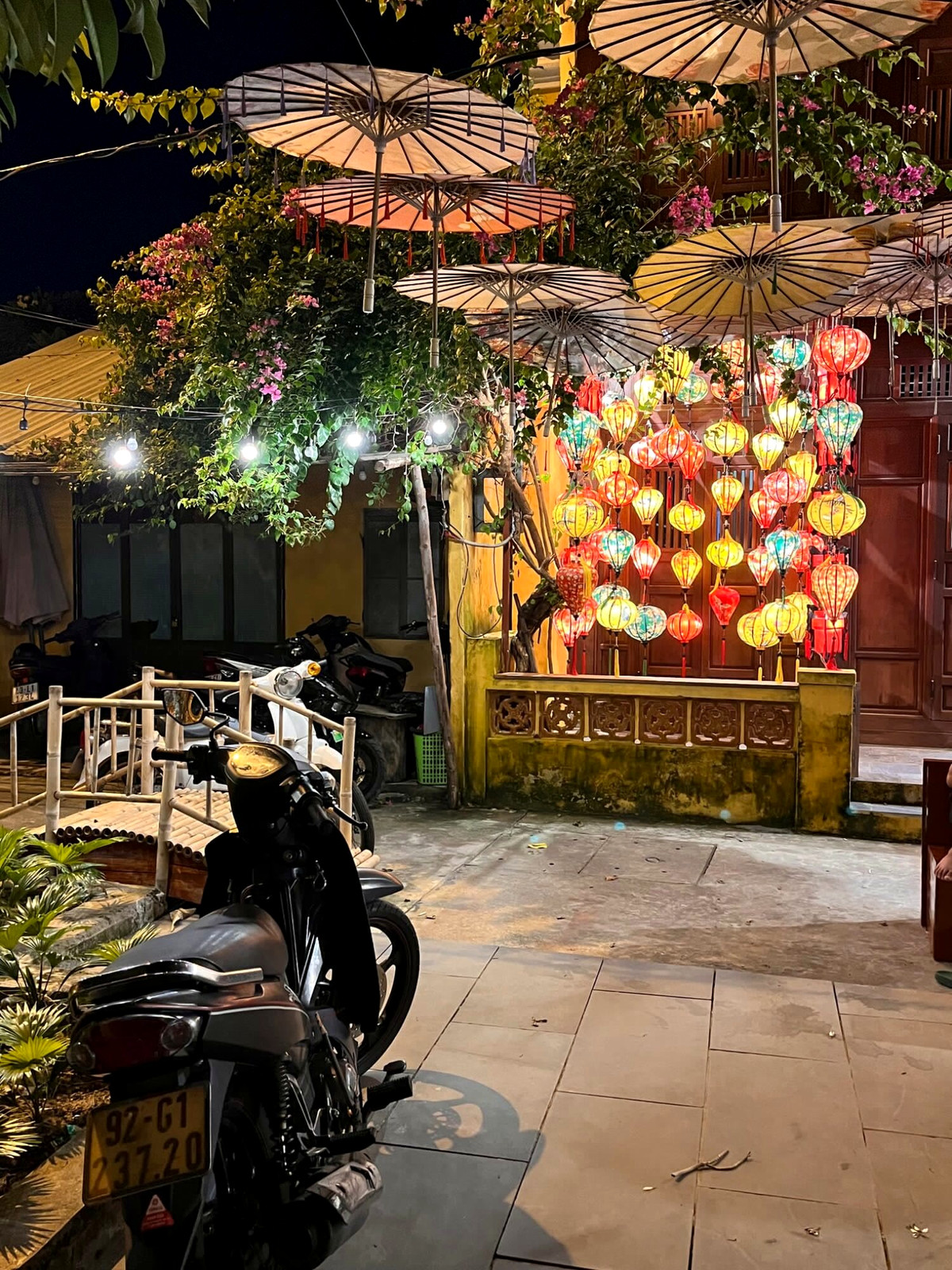 Hoi An cafe entrance with hanging lanterns, plants and a parked bicycle