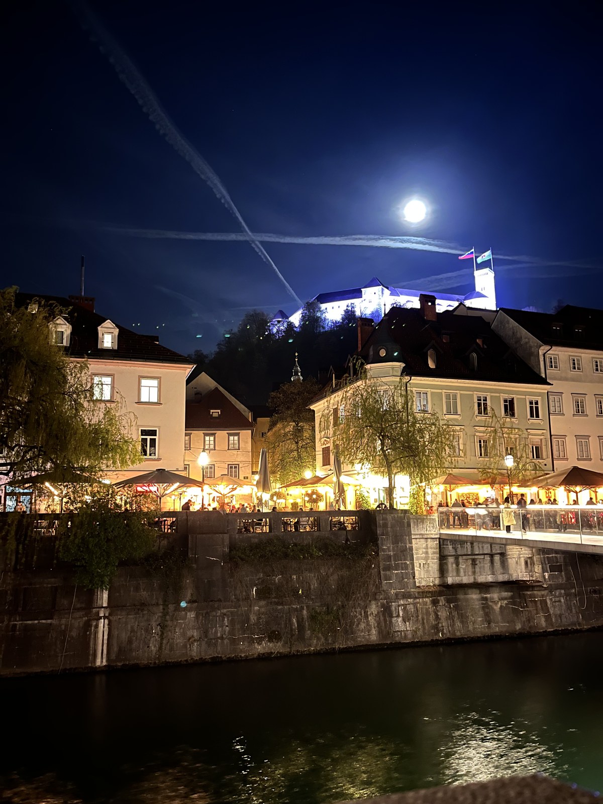 Ljubljana Castle lit up above the old town at night with a full moon overhead