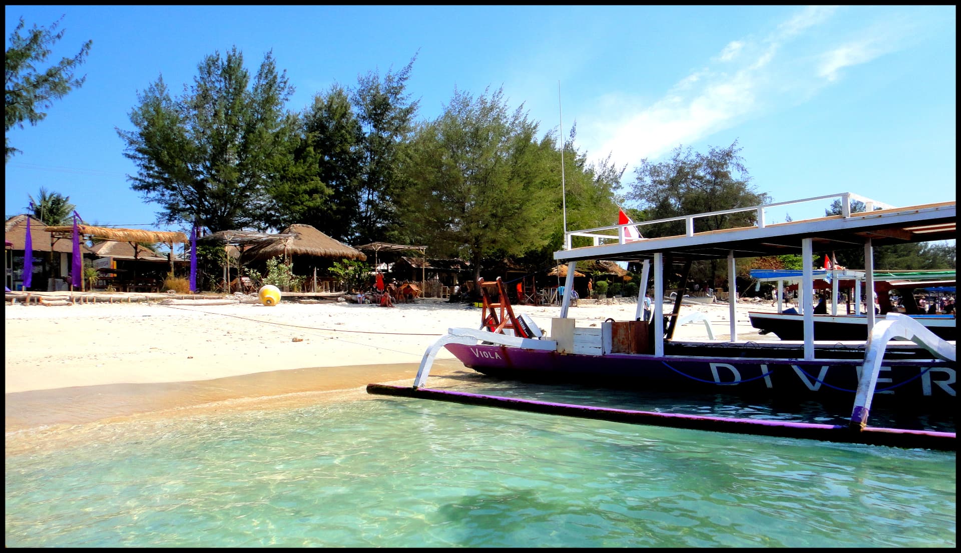 Turquoise shallows and a purple dive boat moored on the white sand shore of Gili Trawangan