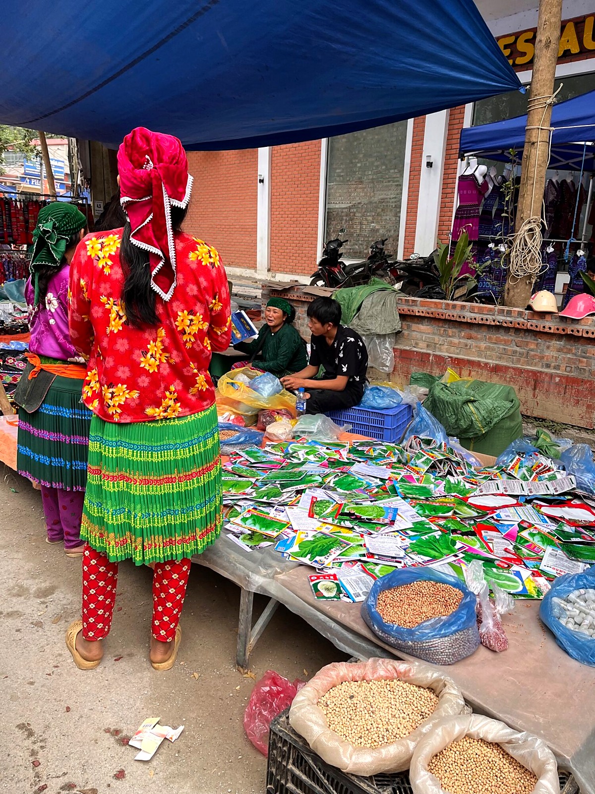 A market shopper in colourful clothing beside a stall of goods