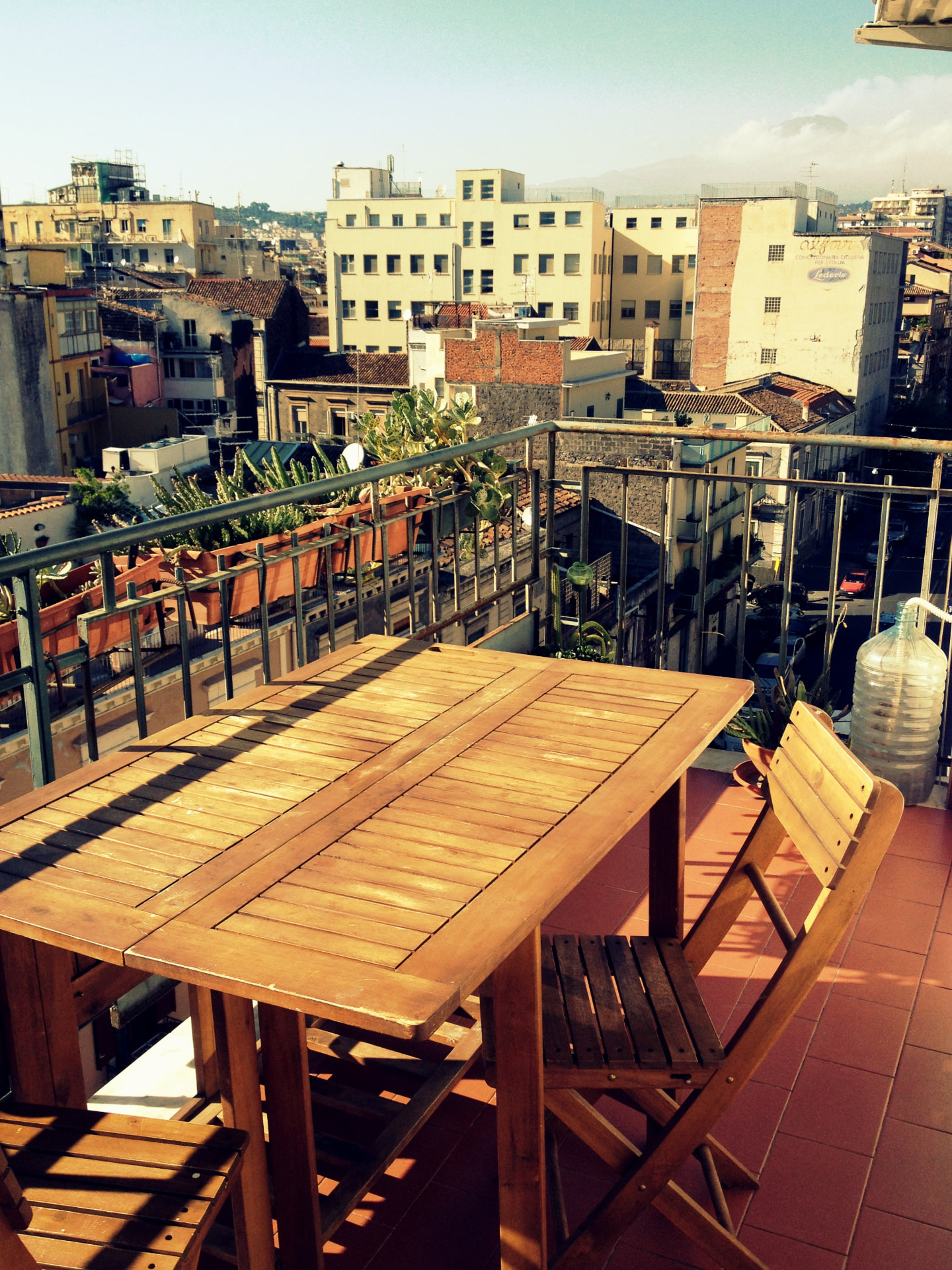 A wooden table on a Catania balcony overlooking rooftops with Mount Etna beyond