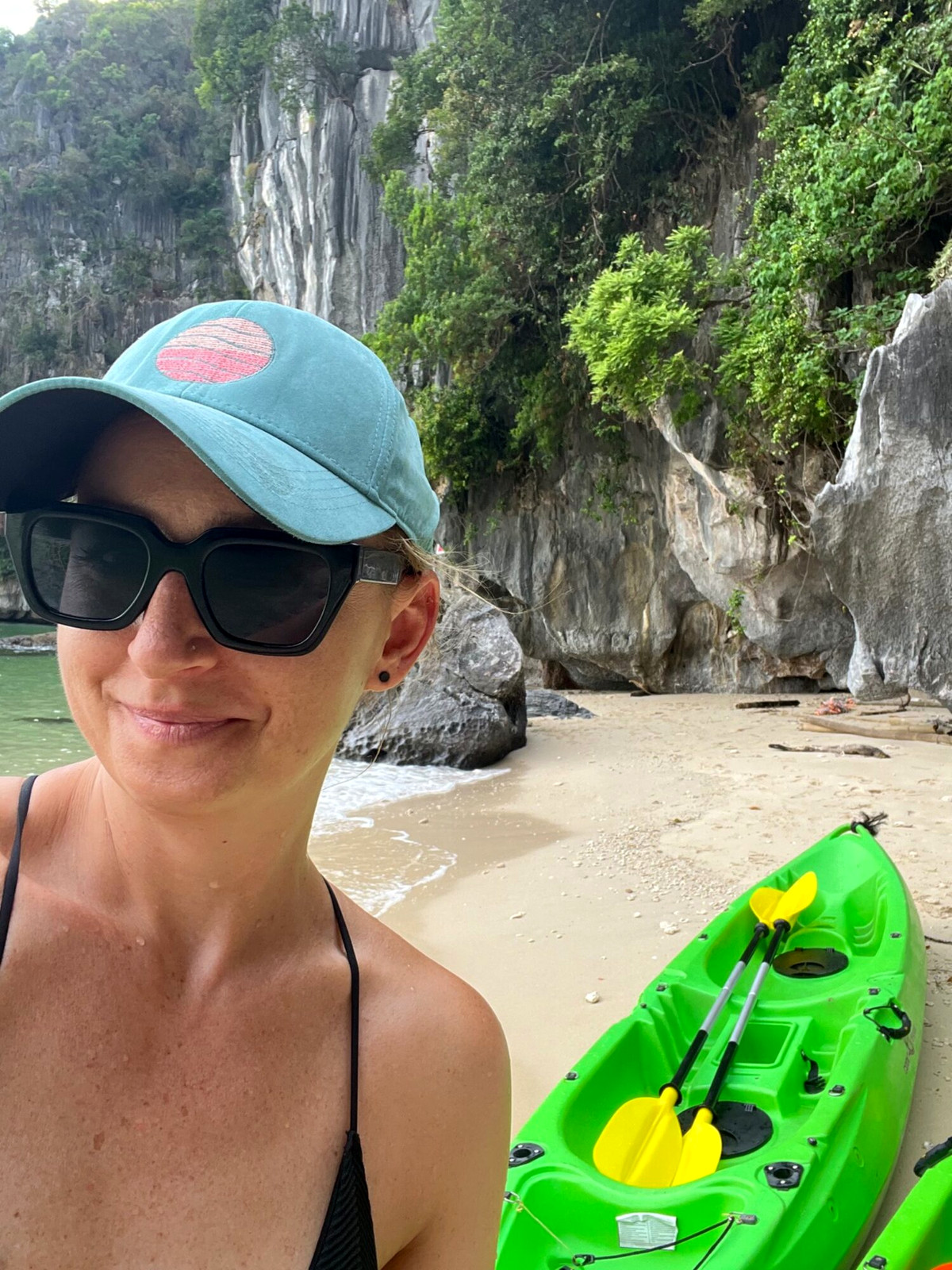 Andreja in a cap and sunglasses beside a green kayak beneath limestone cliffs