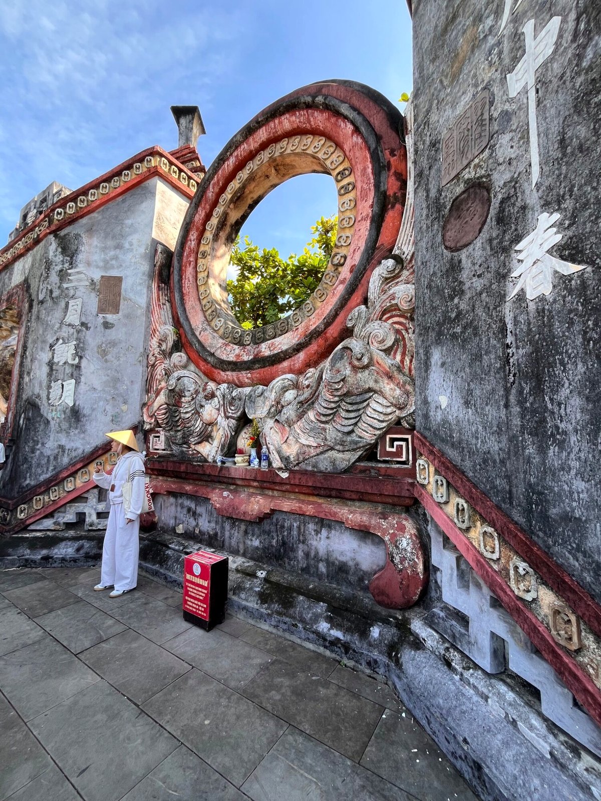 The carved circular screen wall at the Fujian Assembly Hall in Hoi An, with a guide standing in front