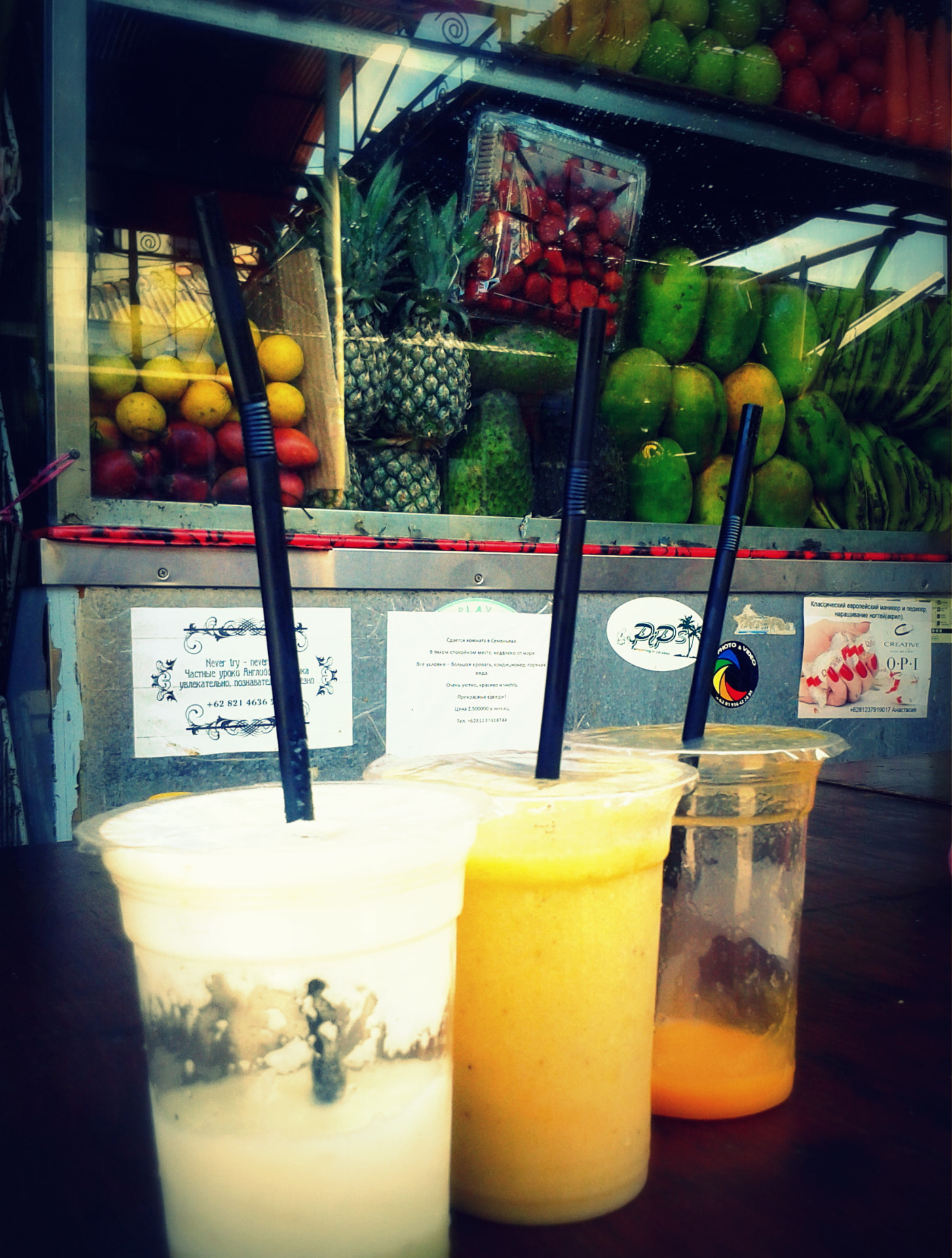 Three fresh fruit smoothies in plastic cups in front of a Bali fruit stall