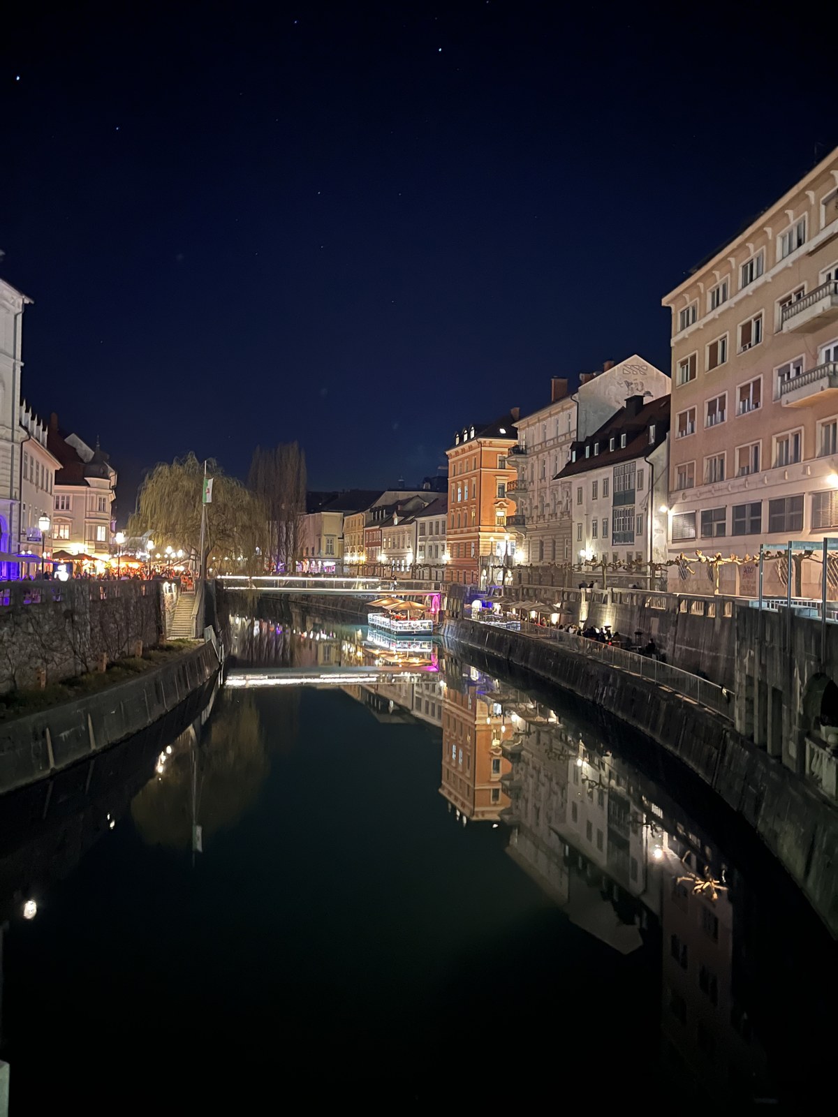 The Ljubljanica river at night reflecting lit-up old town buildings and café terraces