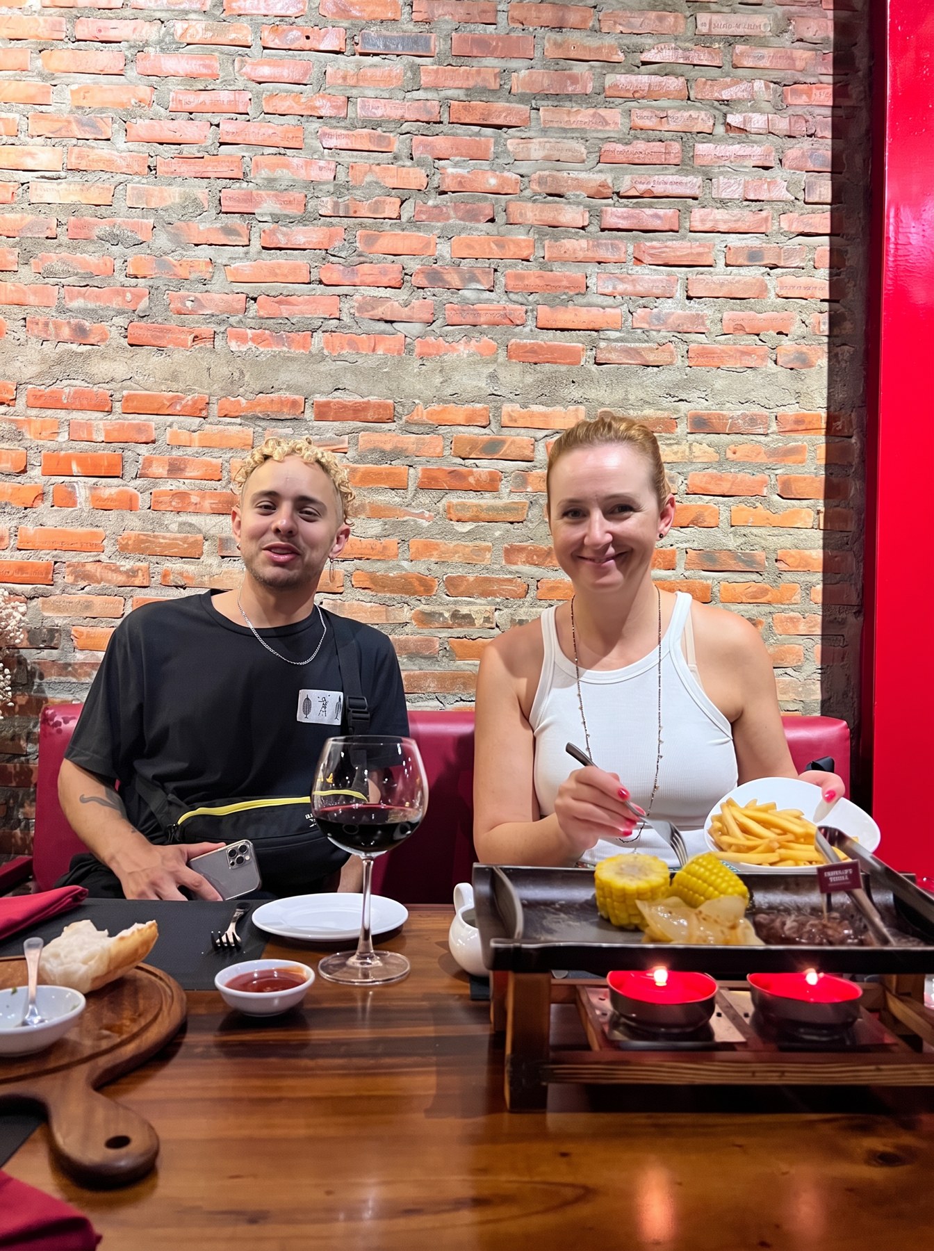 Andreja and Fefe smiling at La Cabana in Da Nang with red wine, fries, corn and steak on a tabletop grill