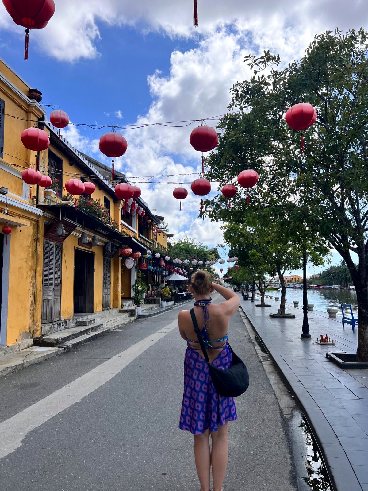 A traveller photographing red lanterns over a yellow-walled Hoi An street by the river