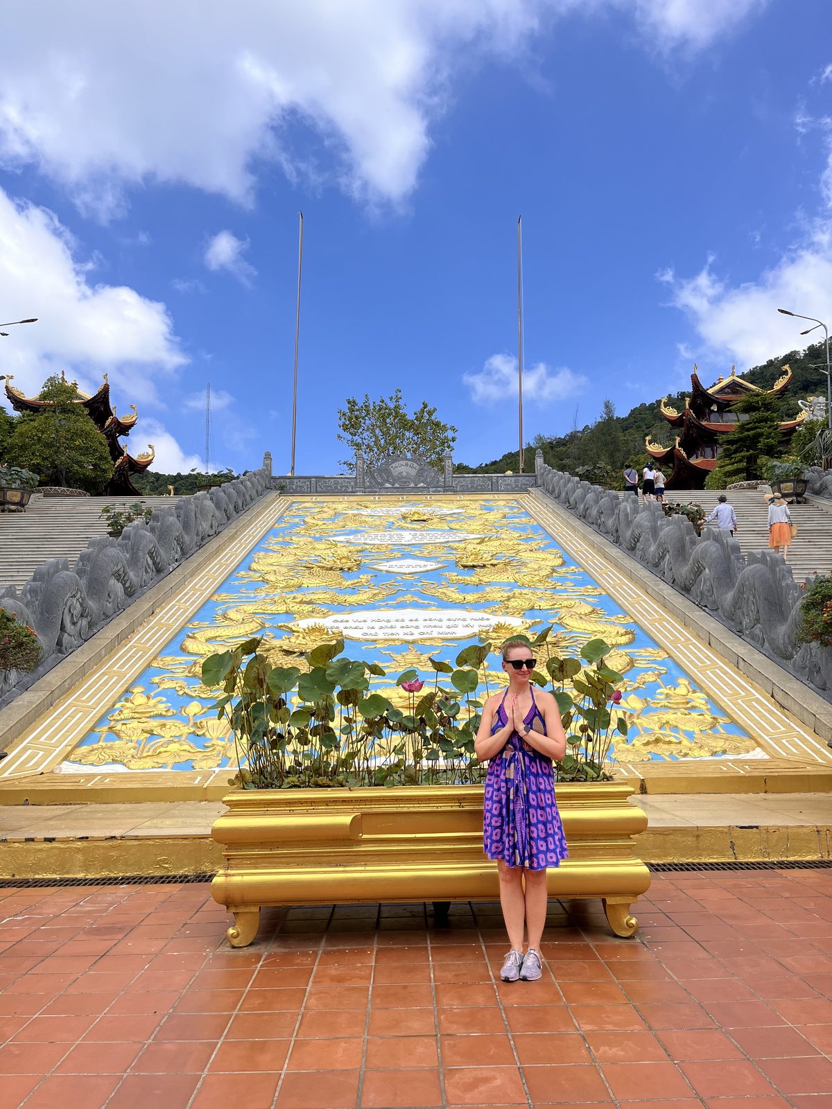 Woman with hands pressed together in front of the golden dragon ramp at Ho Quoc Pagoda on Phu Quoc