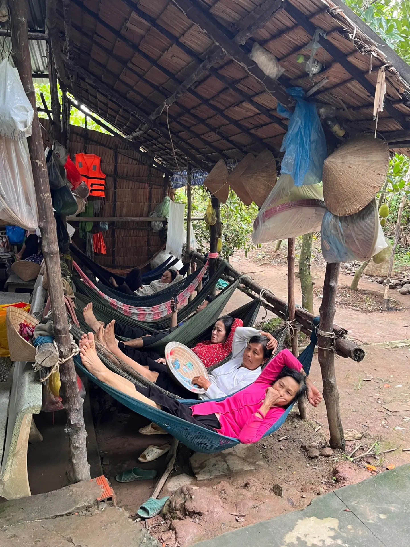 Women resting in hammocks in a thatched shelter along the canal, conical hats hanging on the wall