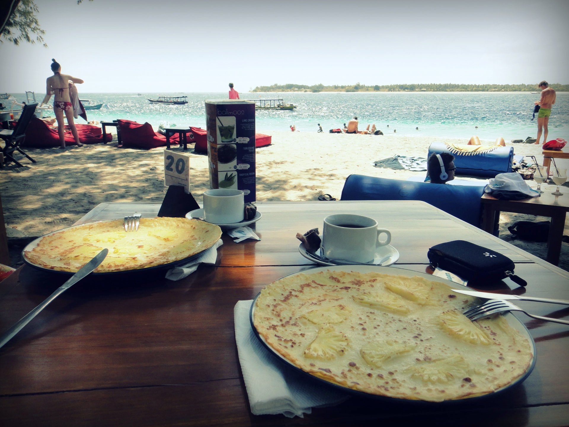 Breakfast crepes and coffee on a wooden table with Gili Trawangan beach and turquoise water in the background