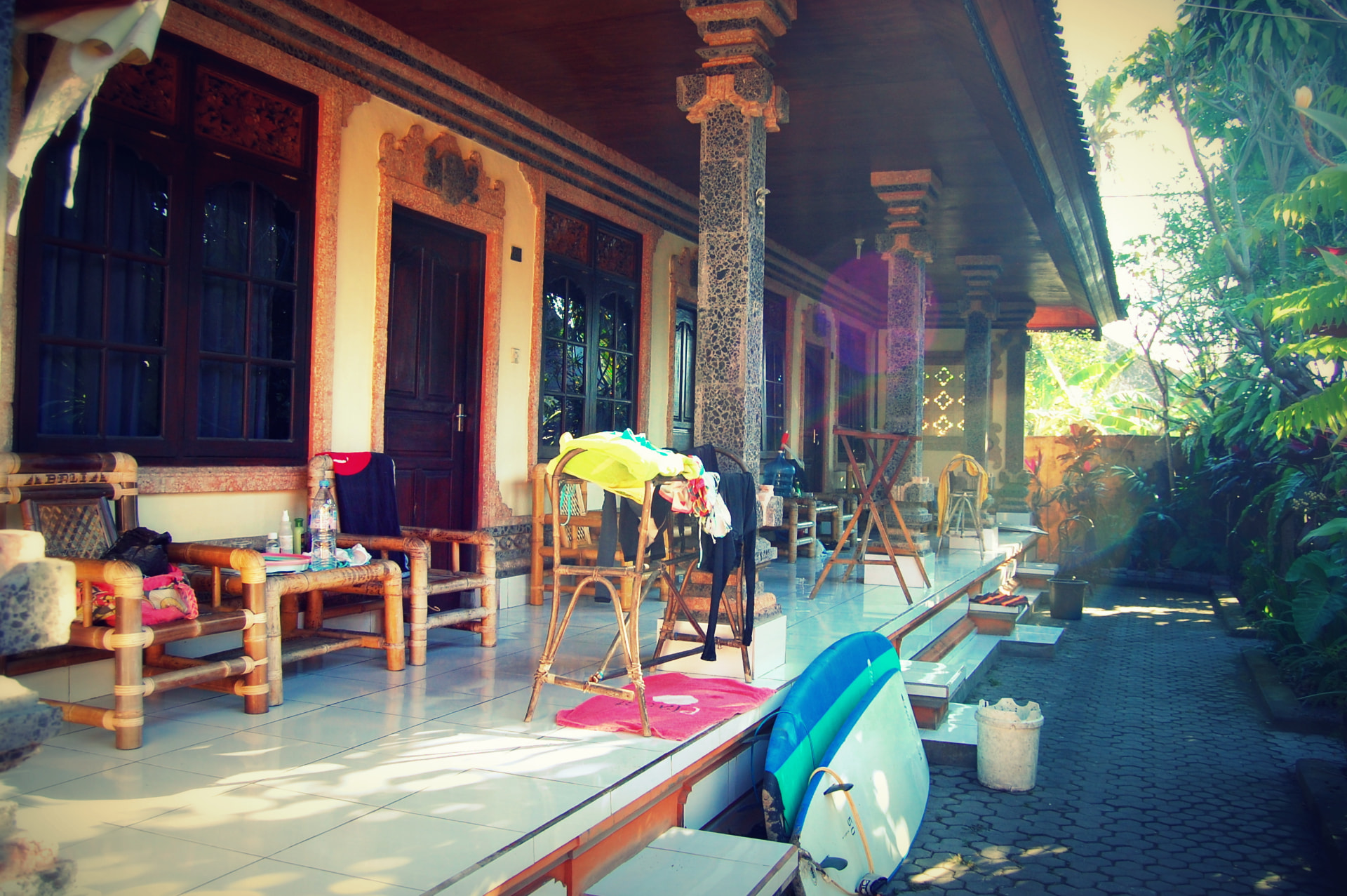 The terrace of a Kuta guesthouse with bamboo chairs, drying surf gear and a surfboard in the morning light