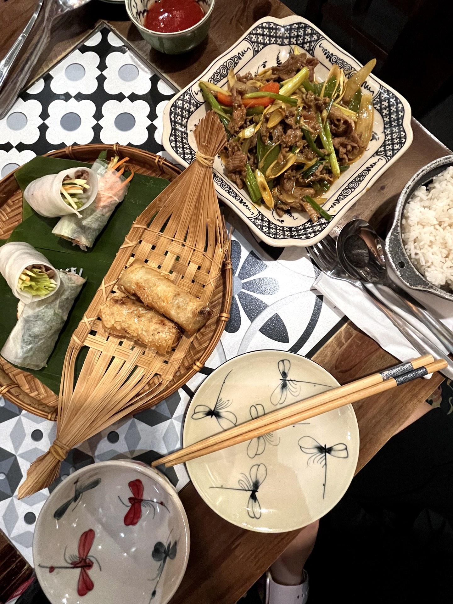 A Vietnamese table spread with spring rolls, stir-fry and dipping sauces