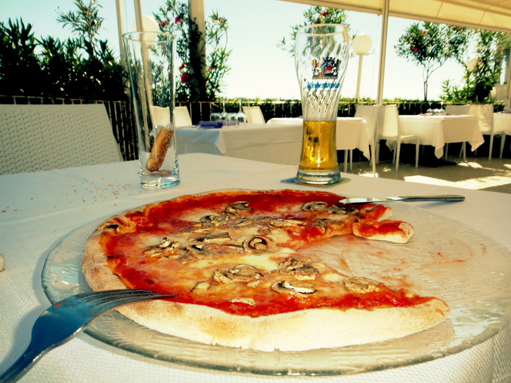 A mushroom pizza and a beer on a terrace table set for one in Sicily