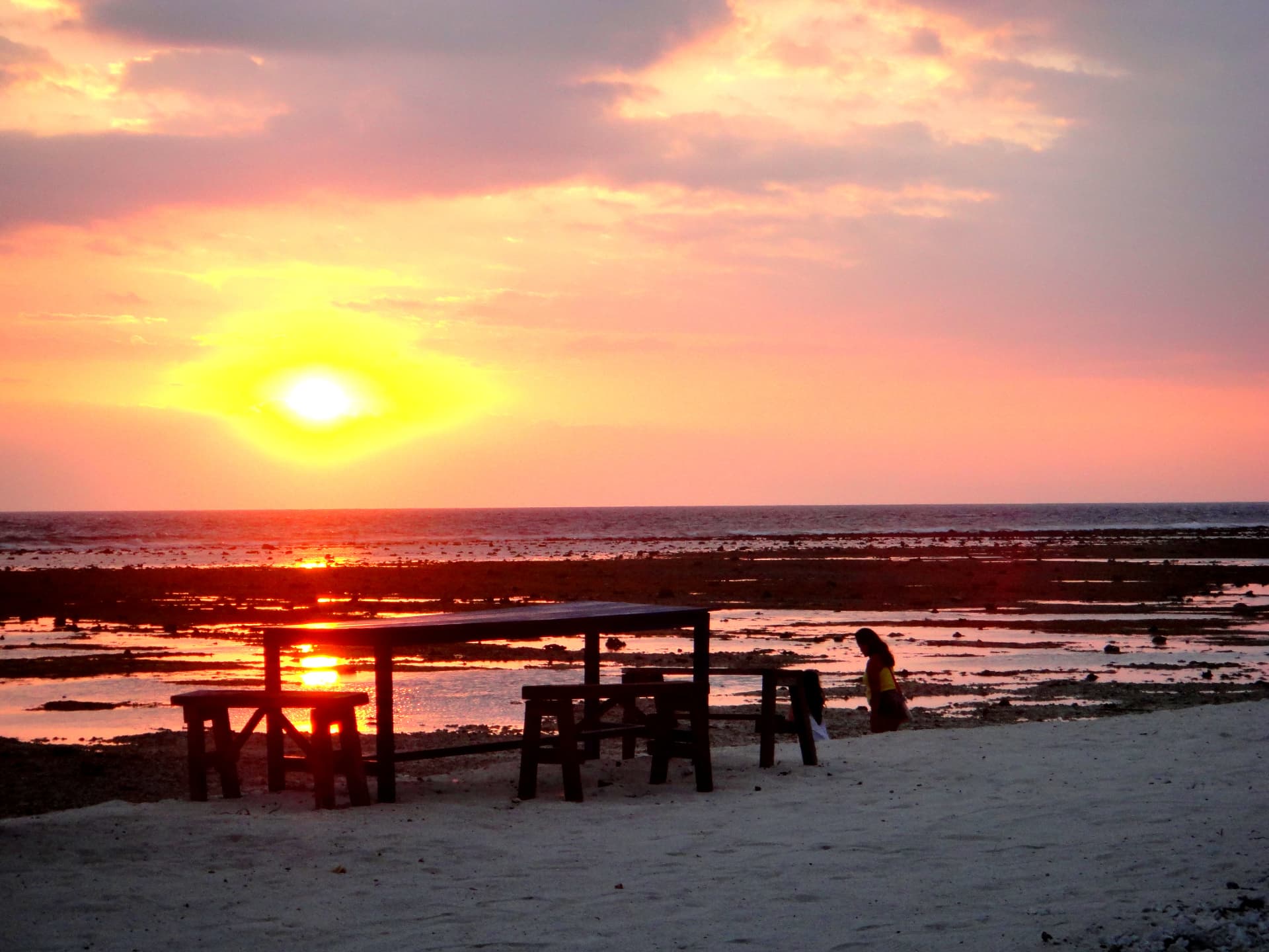 Pink and orange sunset over the reef flats with a wooden beach table in silhouette on Gili Trawangan