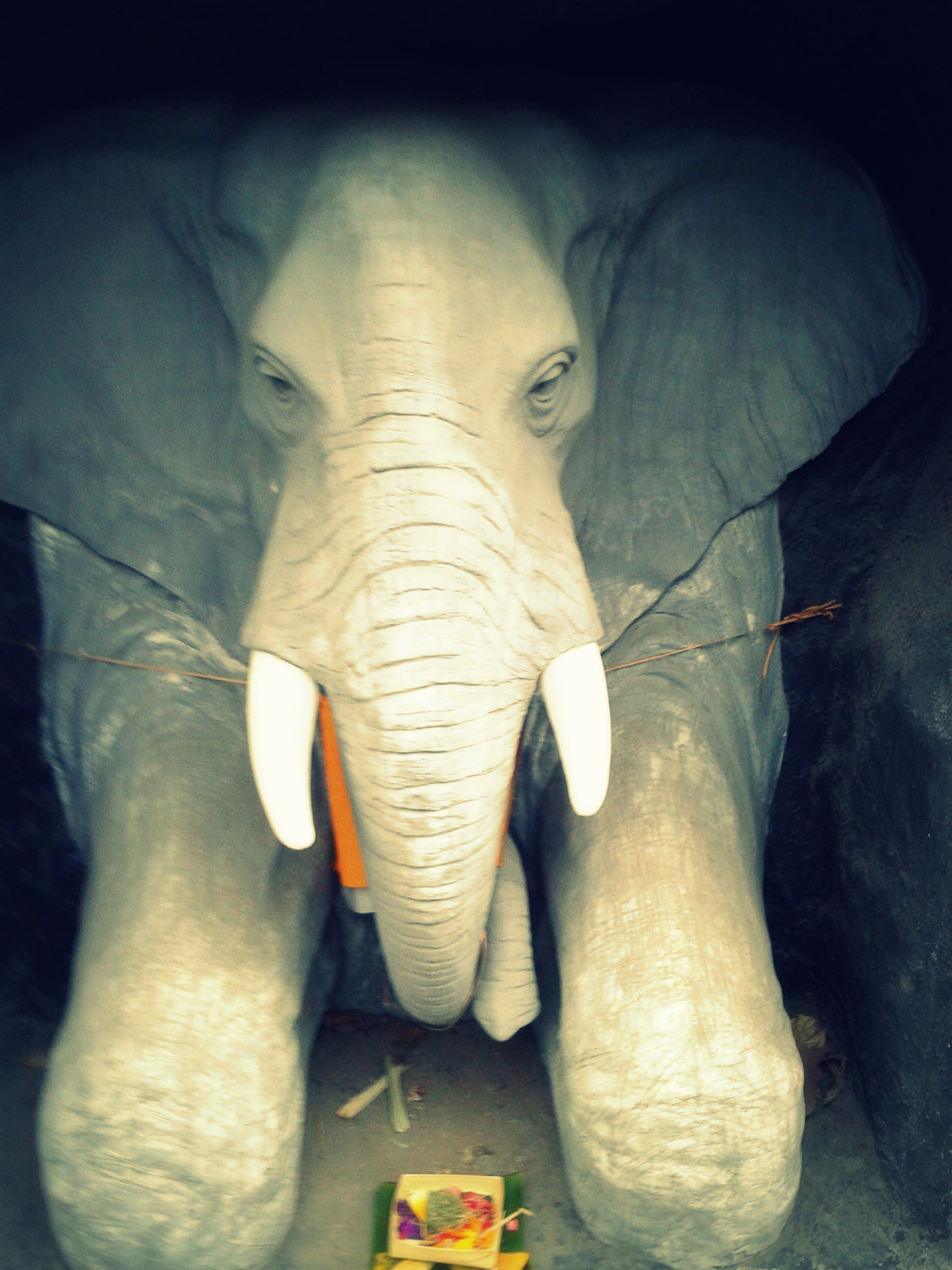 A stone elephant shrine in Bali with a small banana-leaf offering of flowers and incense at its feet