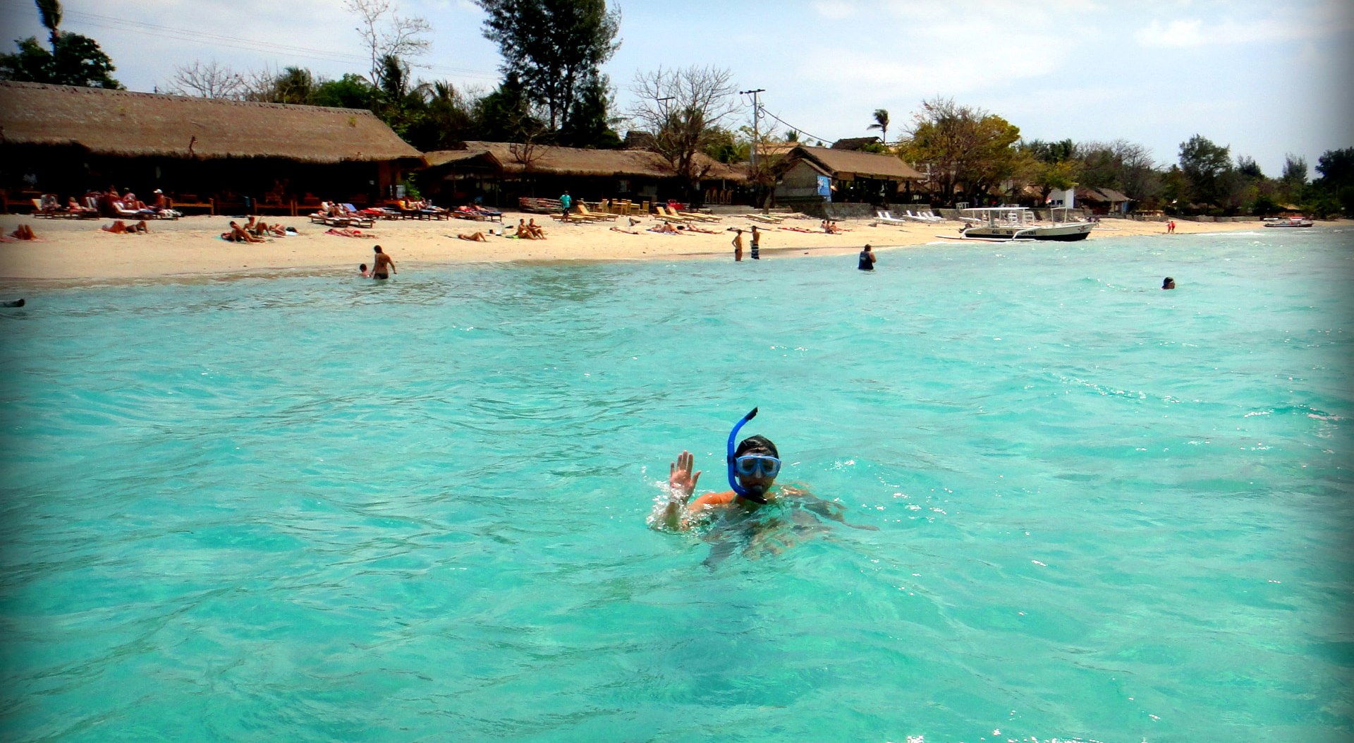 A snorkeler waving from clear turquoise shallow water off a Gili beach