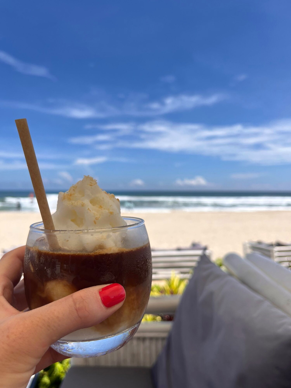Iced drink held at a beach lounge with blue sea and sky beyond