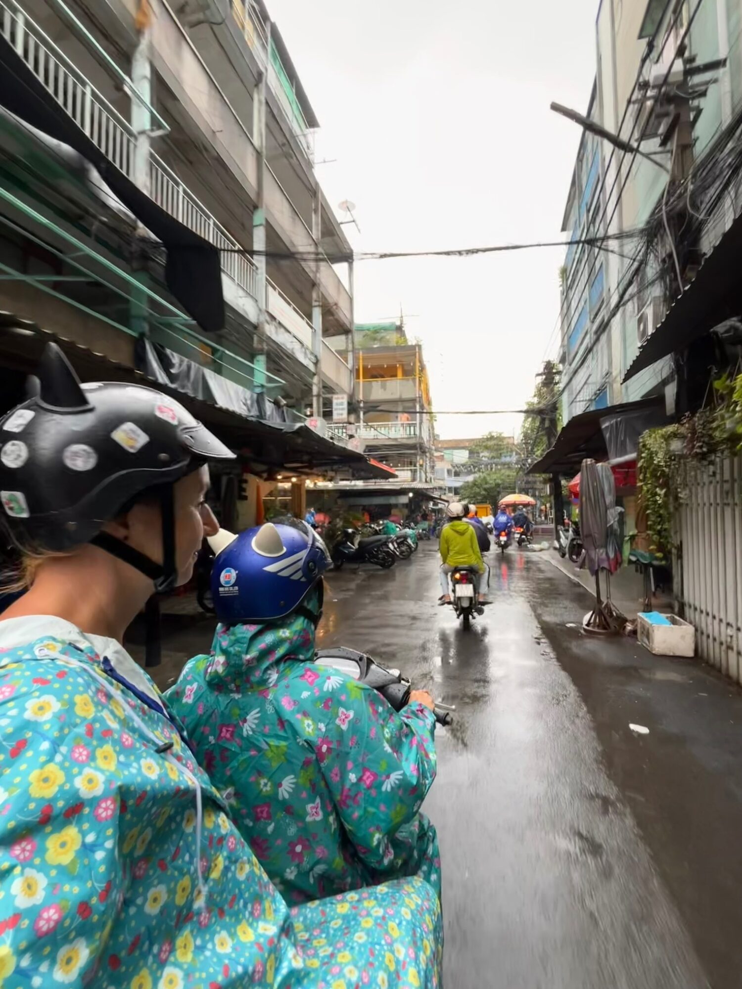 Scooter riders in floral raincoats travelling through a rainy Saigon alley