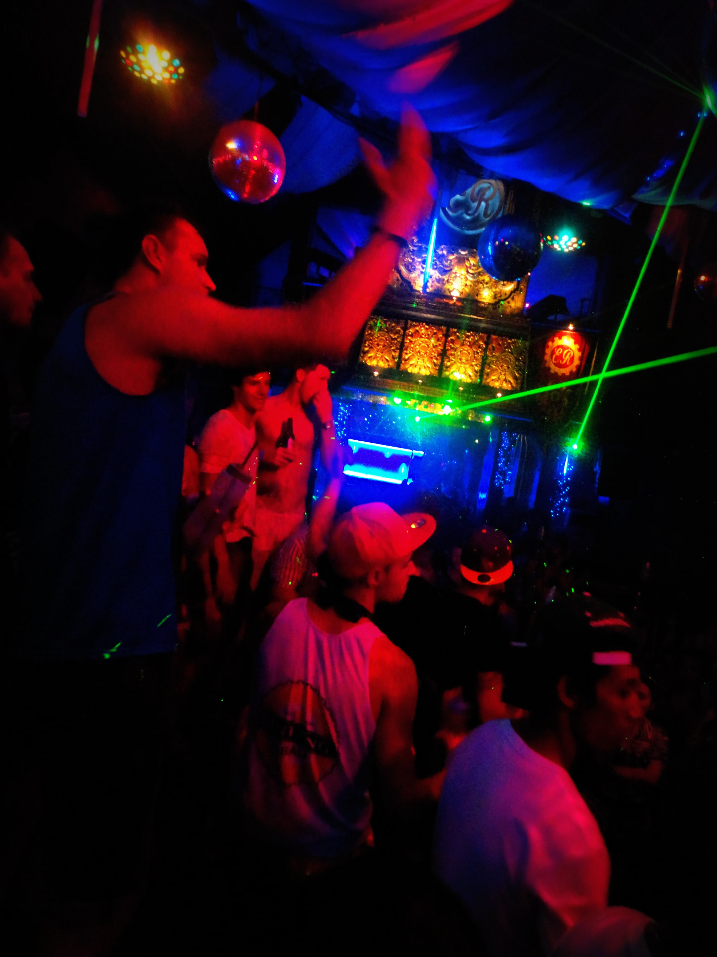 Crowd dancing under disco balls and green laser light in a Kuta club at night