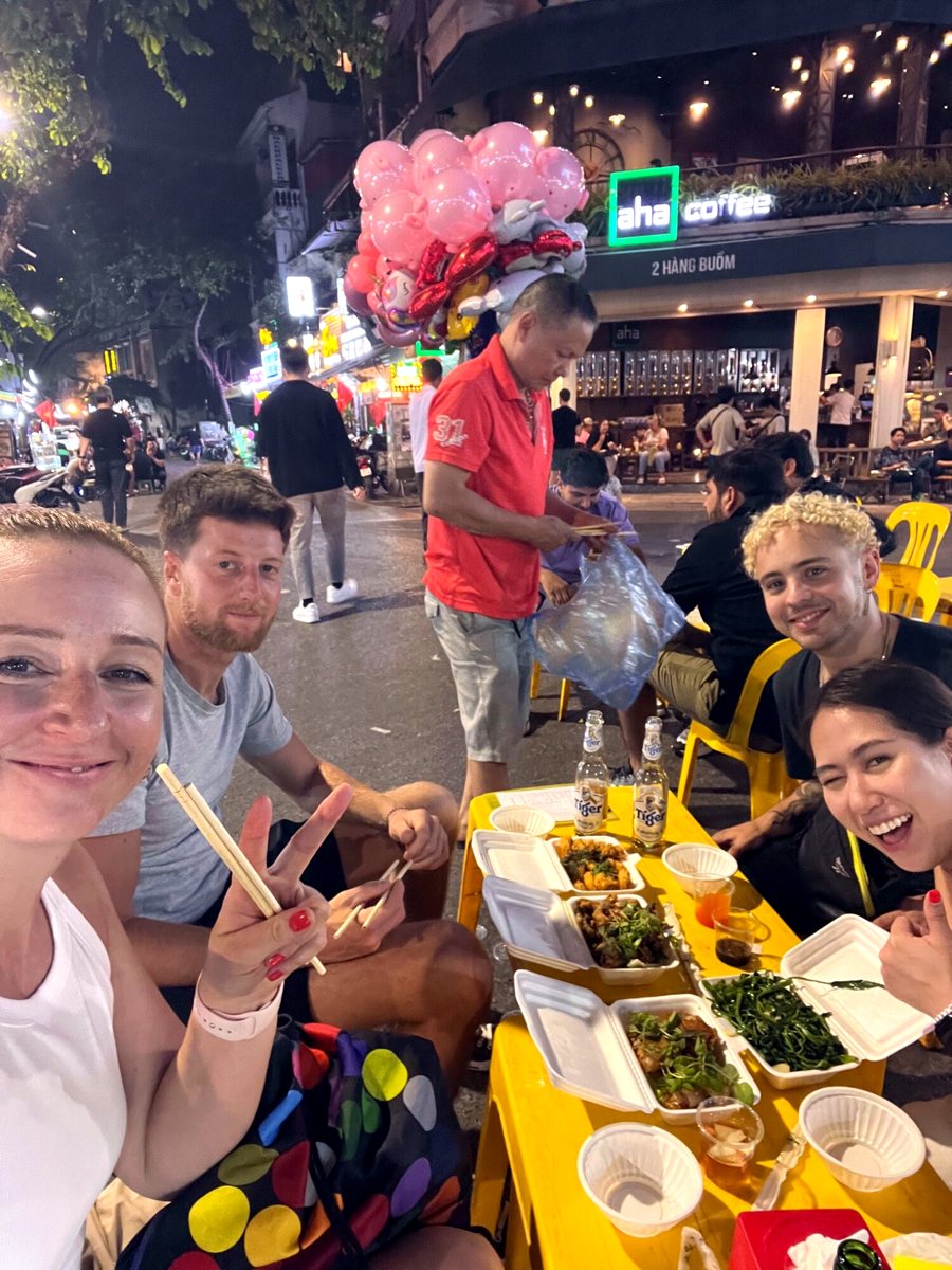 Four friends sharing street food at a yellow table in Hanoi's Old Quarter