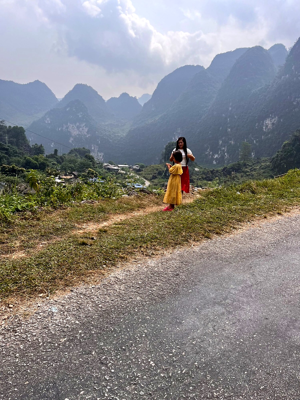 A traveller beside a mountain road with green peaks rising behind her