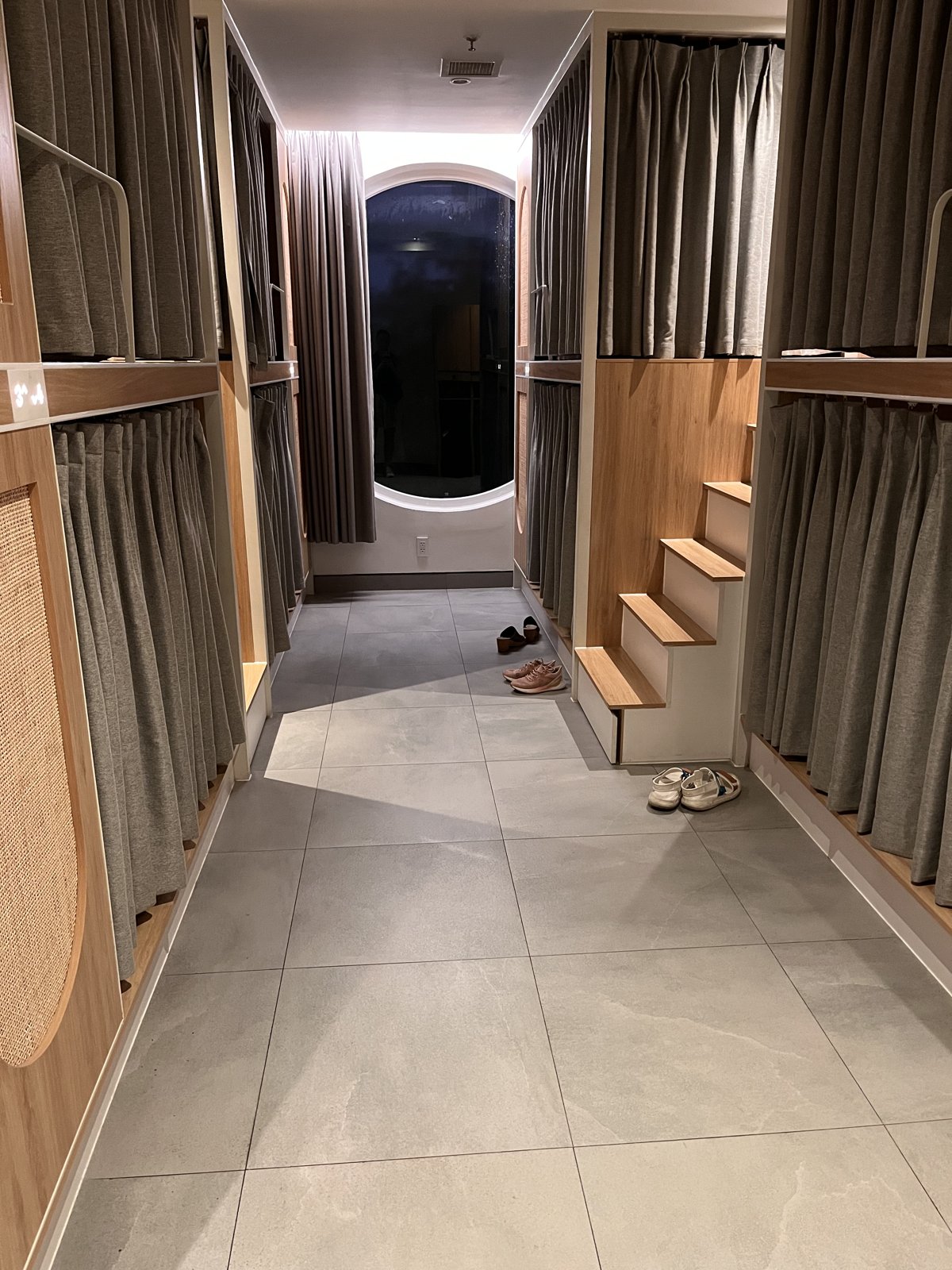 A quiet hostel dorm corridor in Vietnam with curtained pod bunks, wooden steps and shoes left on the floor