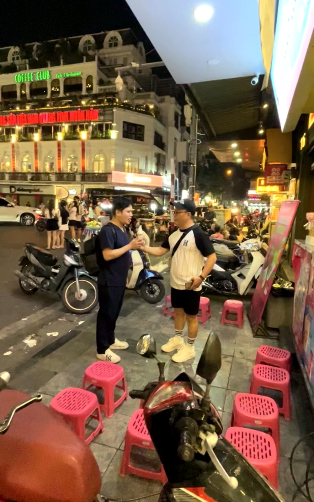 Pink plastic stools on the pavement of a buzzing Hanoi street at night
