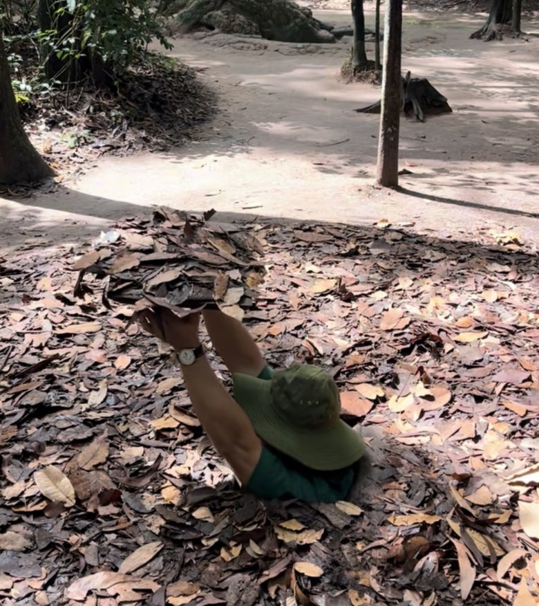 Guide demonstrating a camouflaged trapdoor hidden under leaves at the Cu Chi tunnels