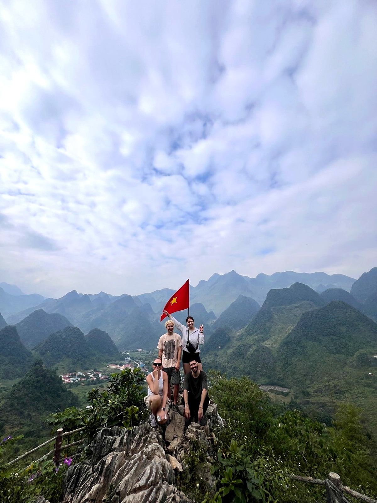 Travellers posing at a mountain viewpoint beneath a Vietnamese flag