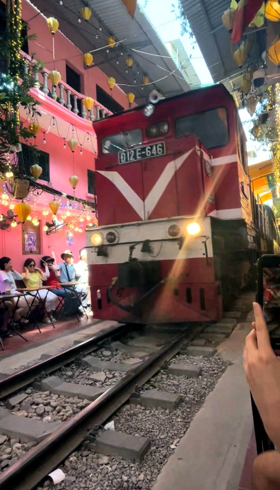 The red train rolling through Hanoi Train Street past the cafés