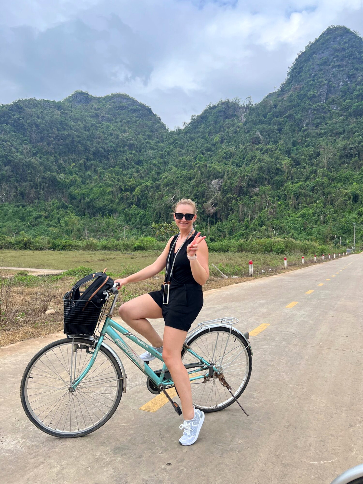 Andreja with a bicycle on Cat Ba island beneath green mountain slopes