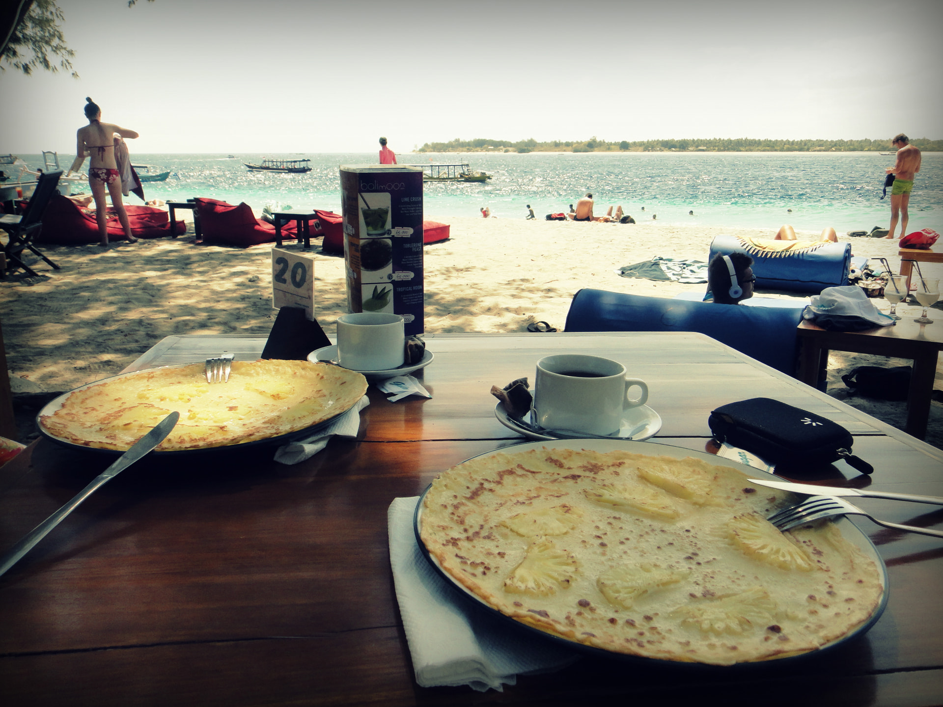 Pineapple pancakes and coffee on a table facing the turquoise water on the Gili Islands