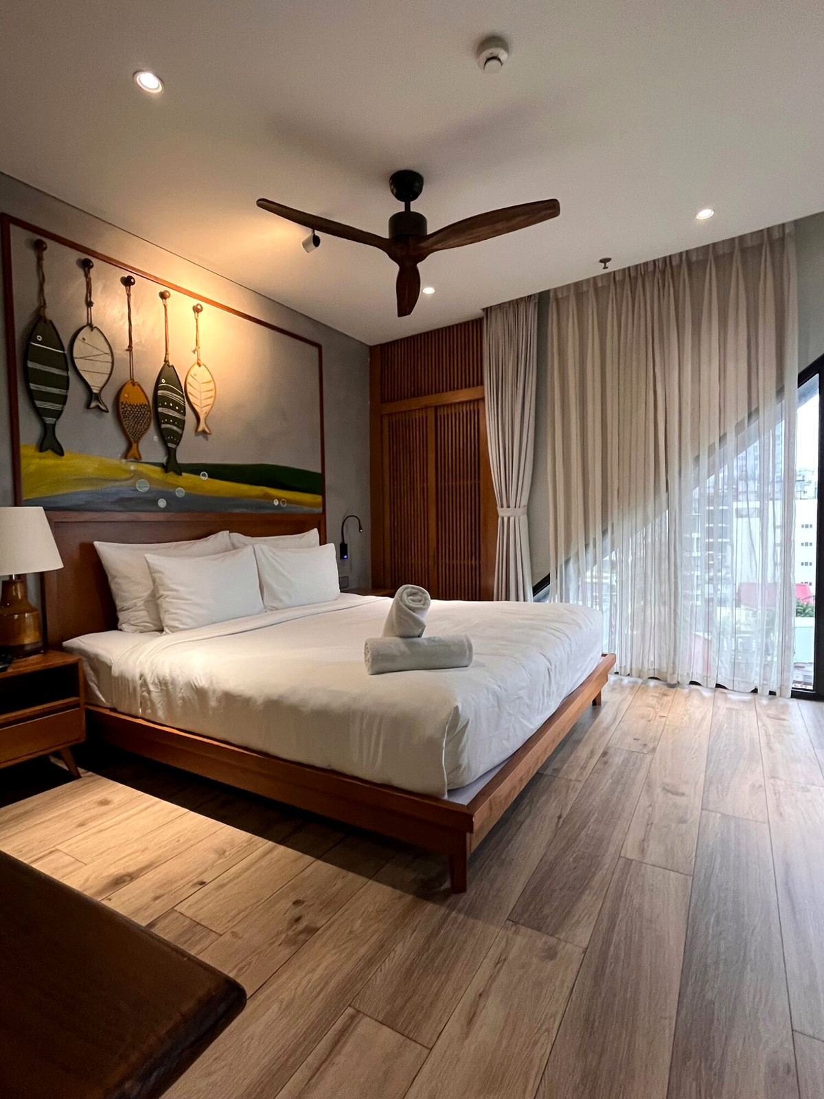 Bright Da Nang hotel room with white bed, wood floor and broad curtained windows