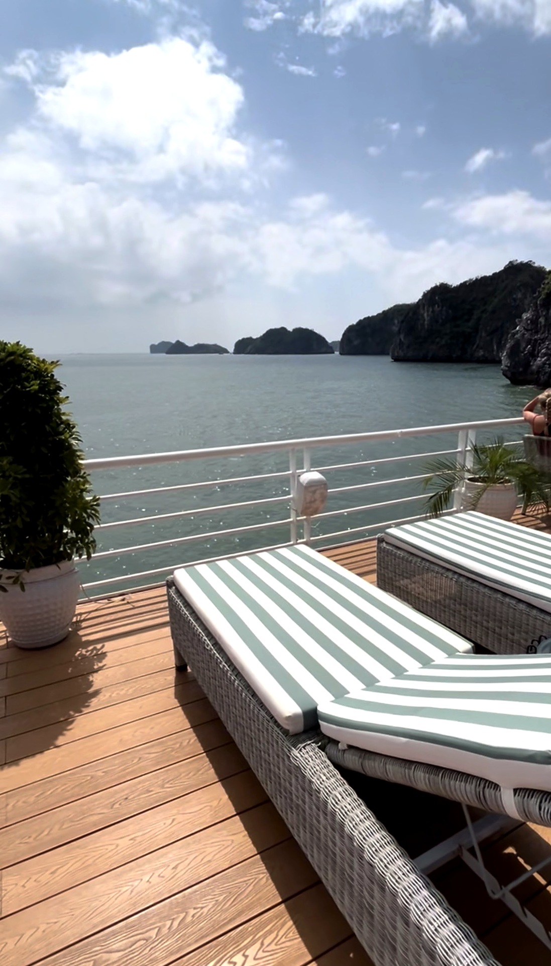 Striped sunbeds on a wooden boat deck overlooking Lan Ha Bay's limestone islands