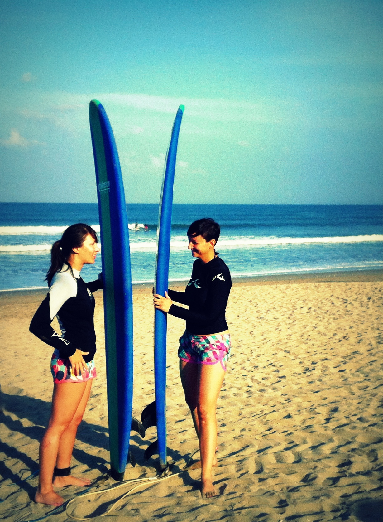 Two surfers holding boards upright on Kuta Beach before a lesson
