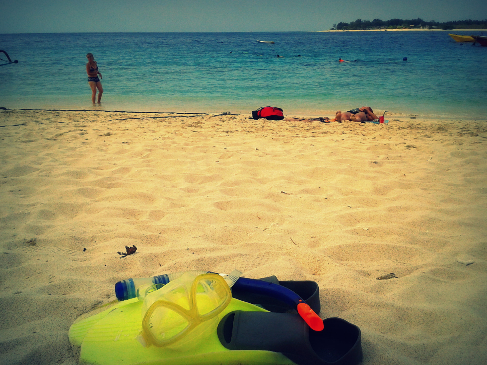 Snorkel mask and fins on white sand with turquoise water and another Gili island behind