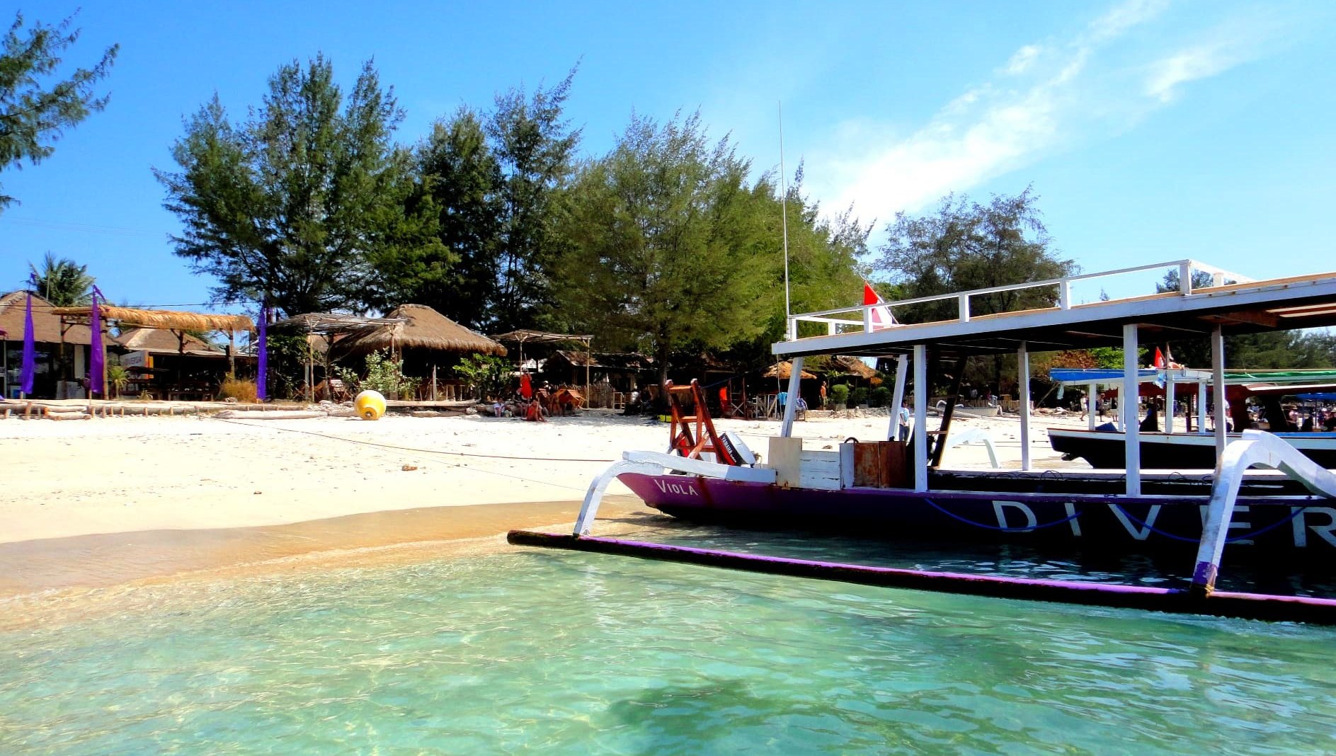 Turquoise shallows and a purple dive boat moored on the white sand shore of Gili Trawangan