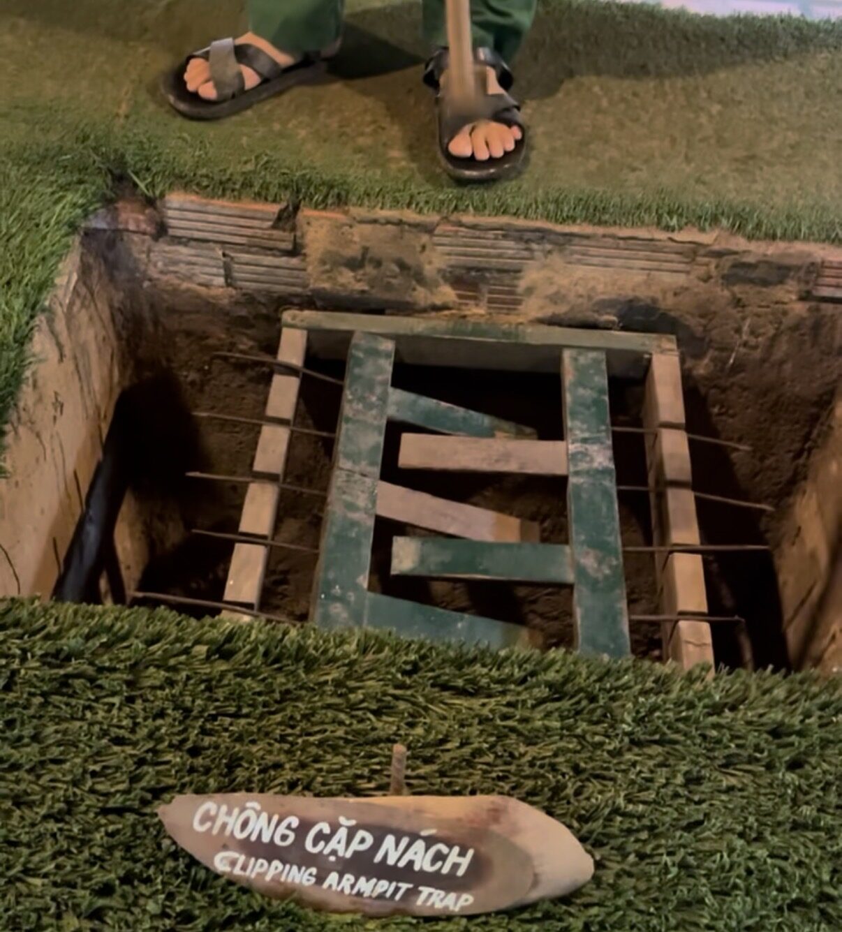 Demonstration of a spiked pit trap at the Cu Chi tunnels, with a sign reading 'Clipping Armpit Trap'