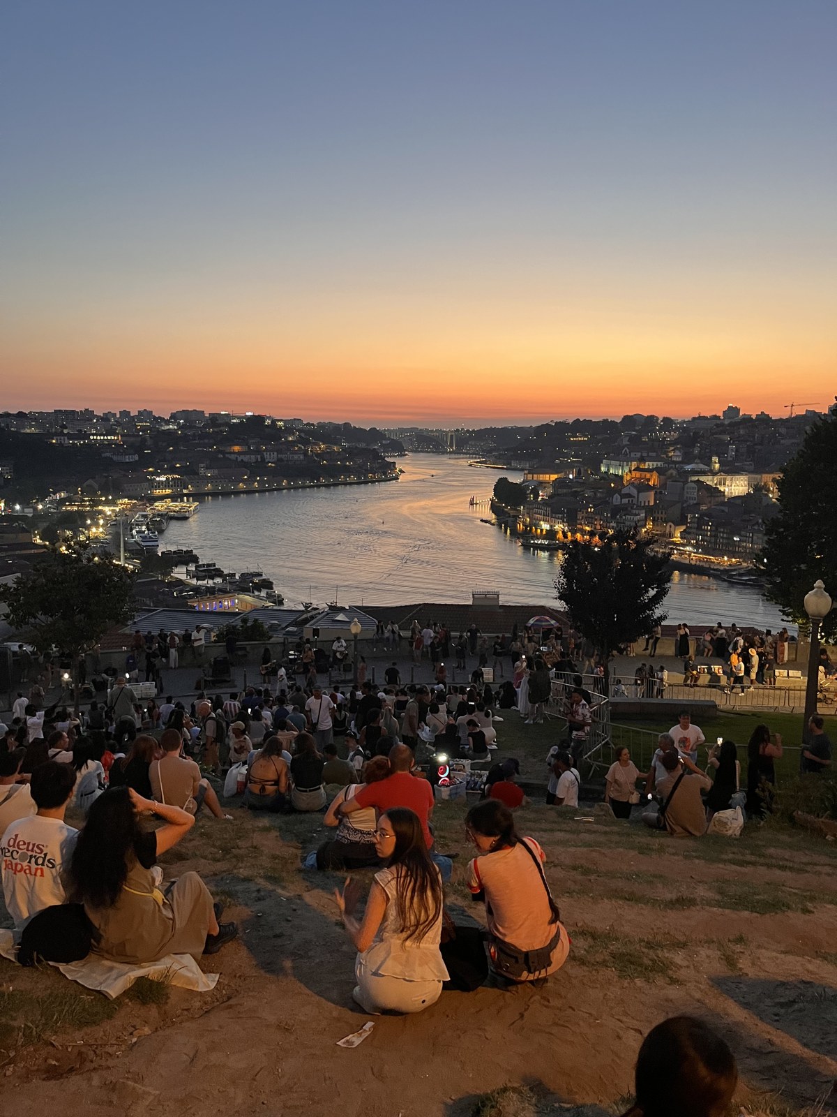 Crowds sitting on a Gaia hillside watching sunset over the Douro river and Porto