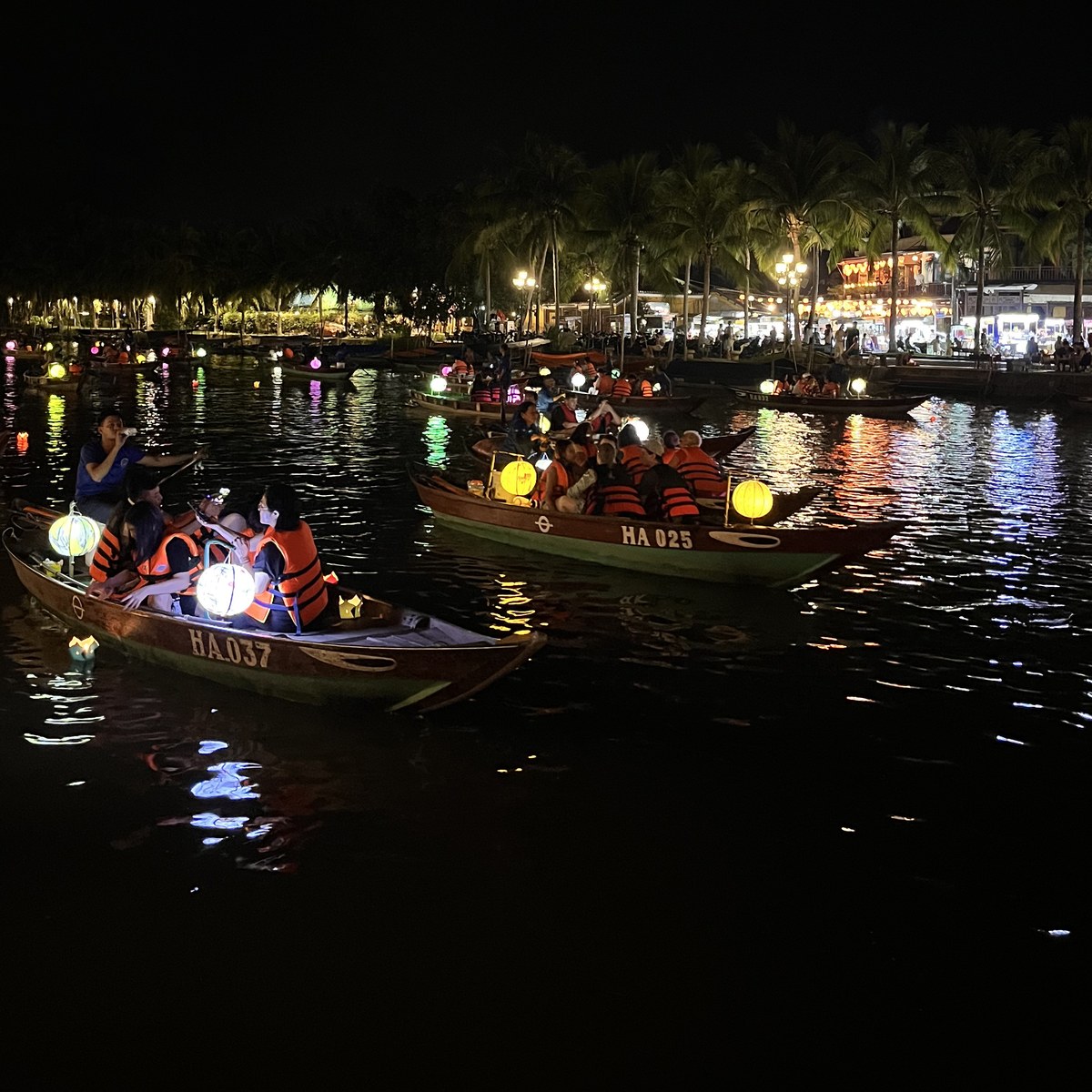 Night boats loaded with passengers and glowing lanterns on the river in Hoi An