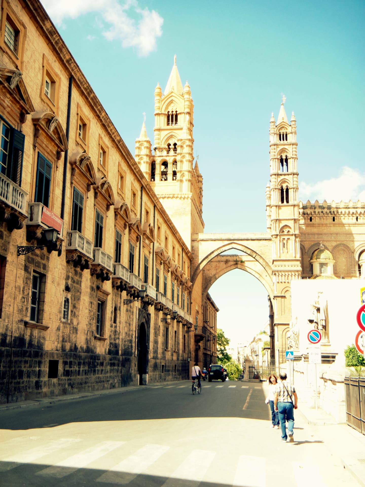 Palermo Cathedral's spires and arch seen from the street on a bright afternoon