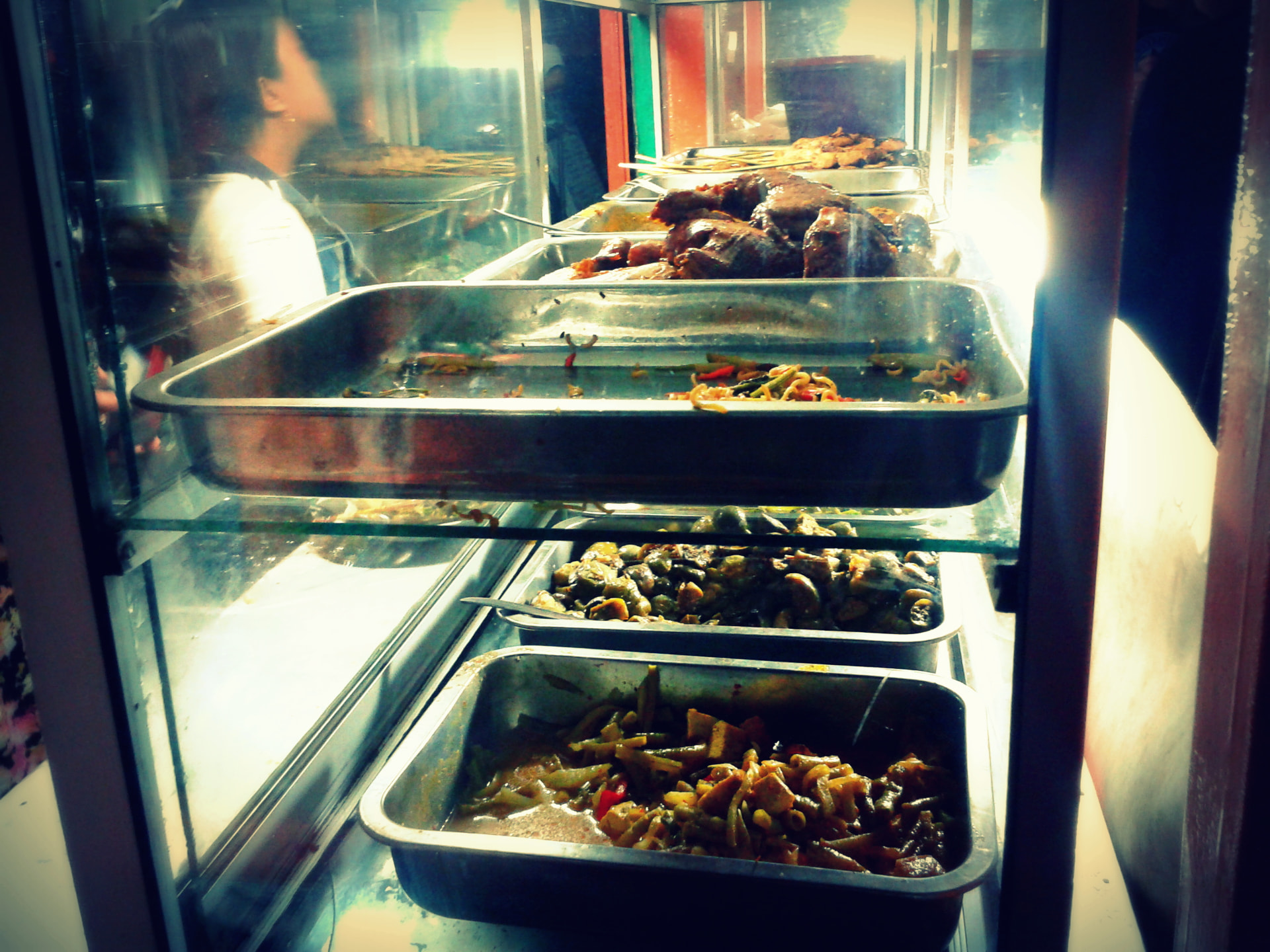 Warm trays of curries, satay and vegetables in a glass night market food cabinet in Kuta, Bali