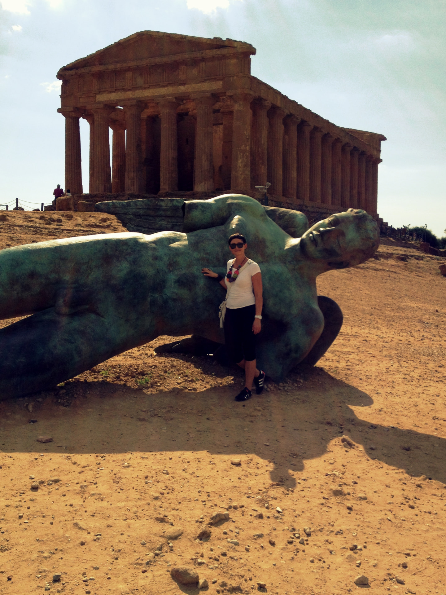 A woman standing beside the fallen Icarus bronze statue in front of a Greek temple in Agrigento