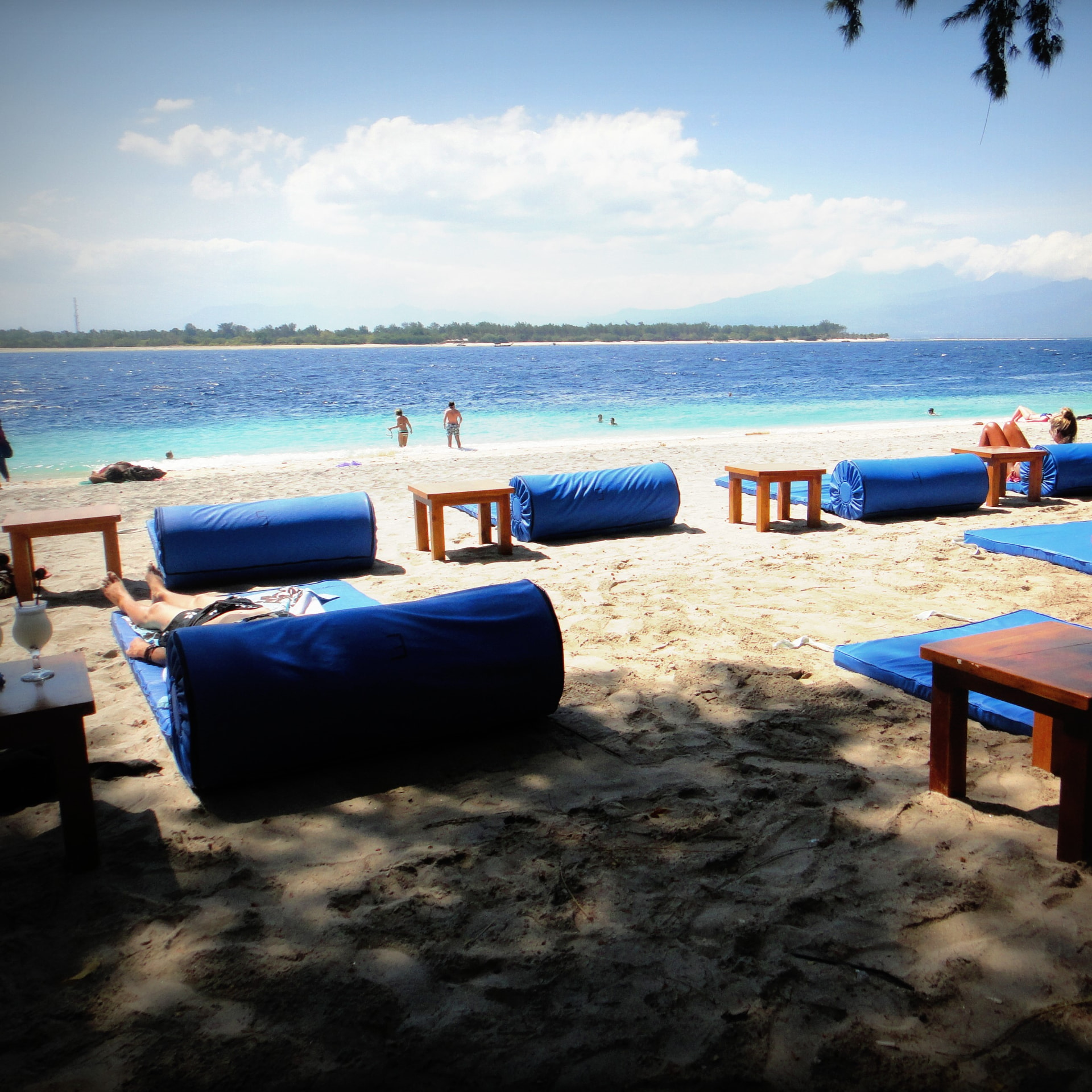 Blue beach beanbags and low wooden tables on white sand facing turquoise water on Gili Trawangan