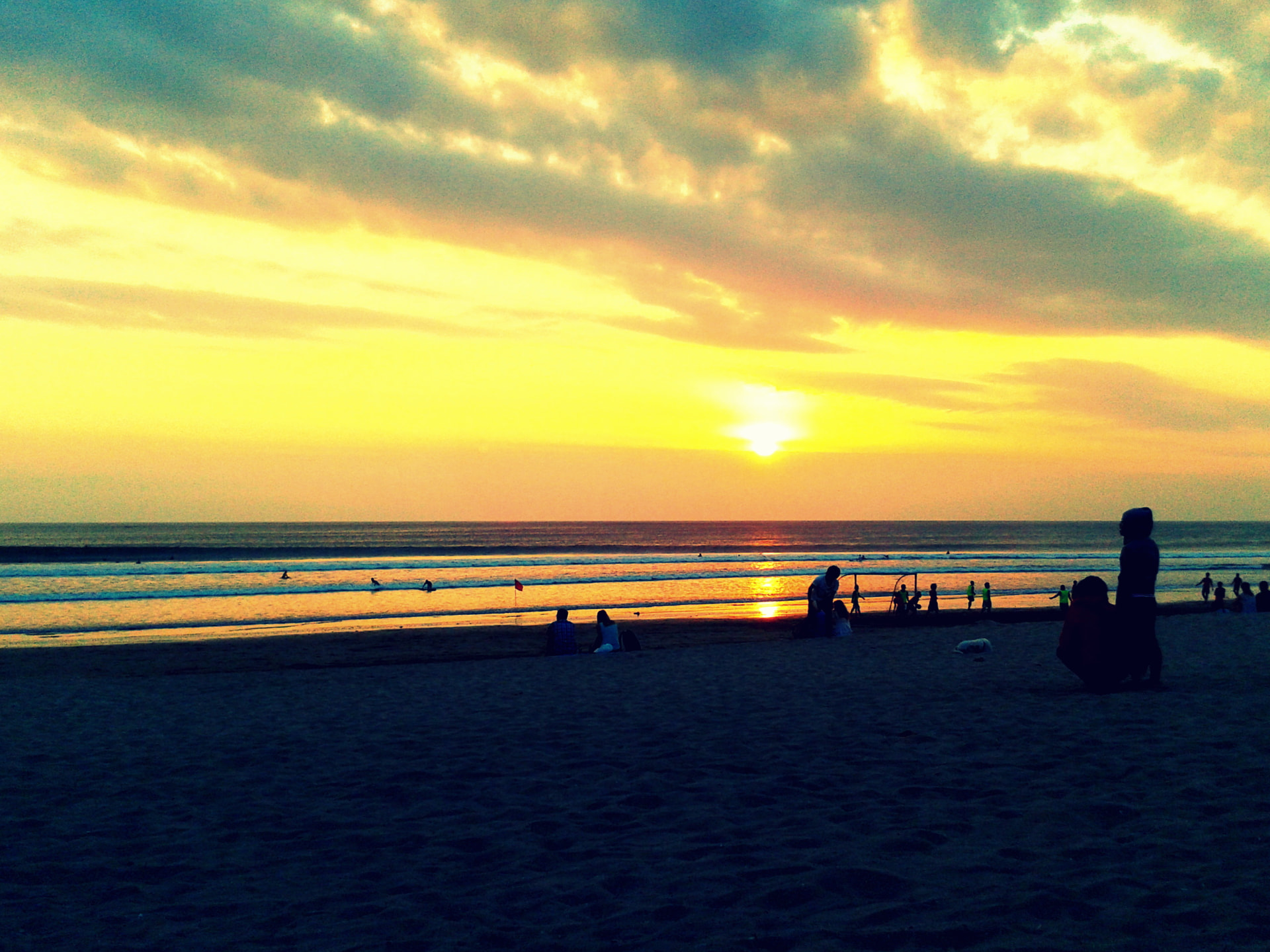 Golden sunset over the ocean on a Bali beach with surfers and people sitting on the sand