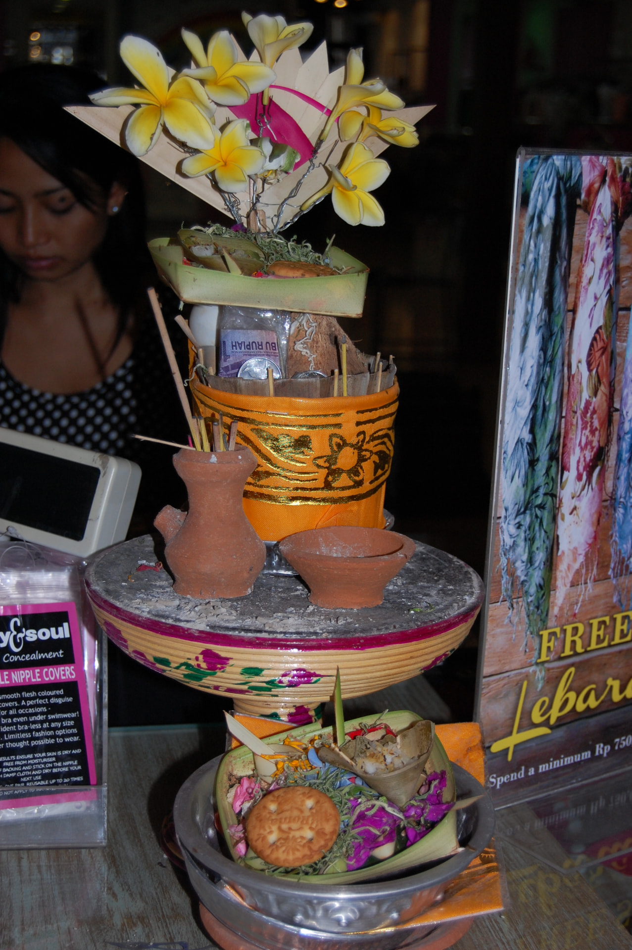 A Balinese offering with frangipani flowers, incense and rupiah notes on a clothes shop counter in Kuta